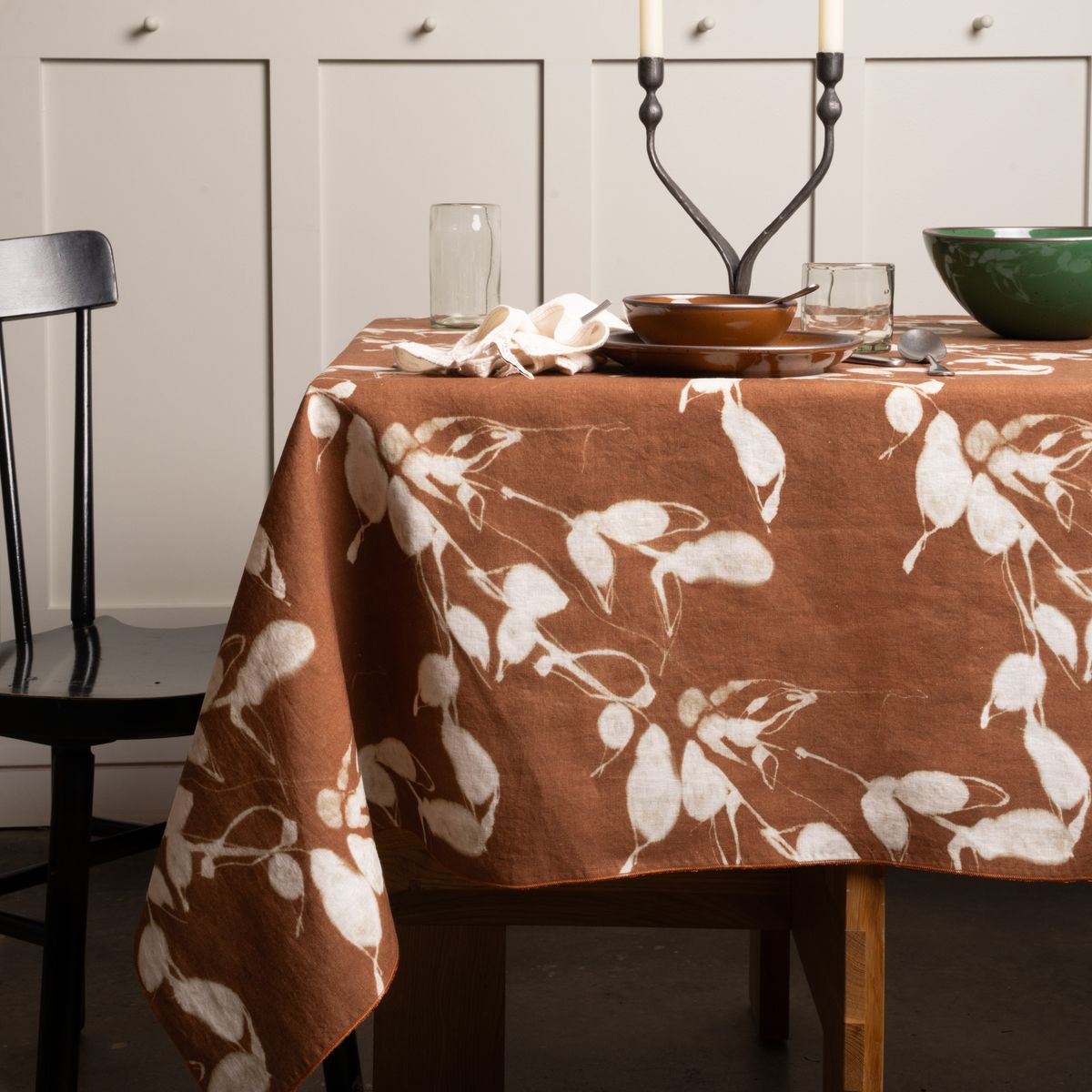 Brown tablecloth with white leaf pattern, styled on a dining table with dinnerware, glassware, and candles.