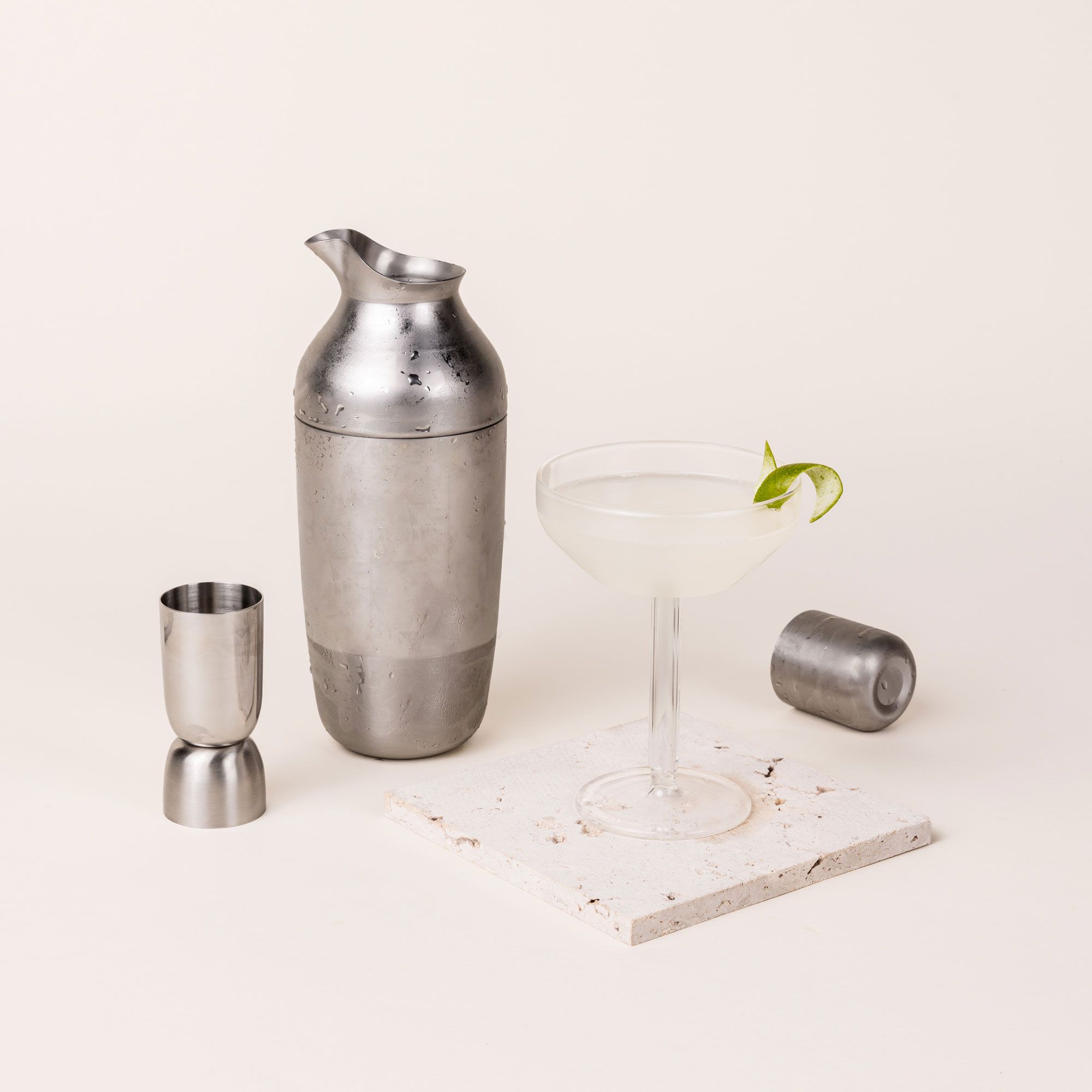 The Mescola Cocktail Set (including a stainless steel shaker, jigger, and cocktail spoon) with a fresh martini in a coupe glass