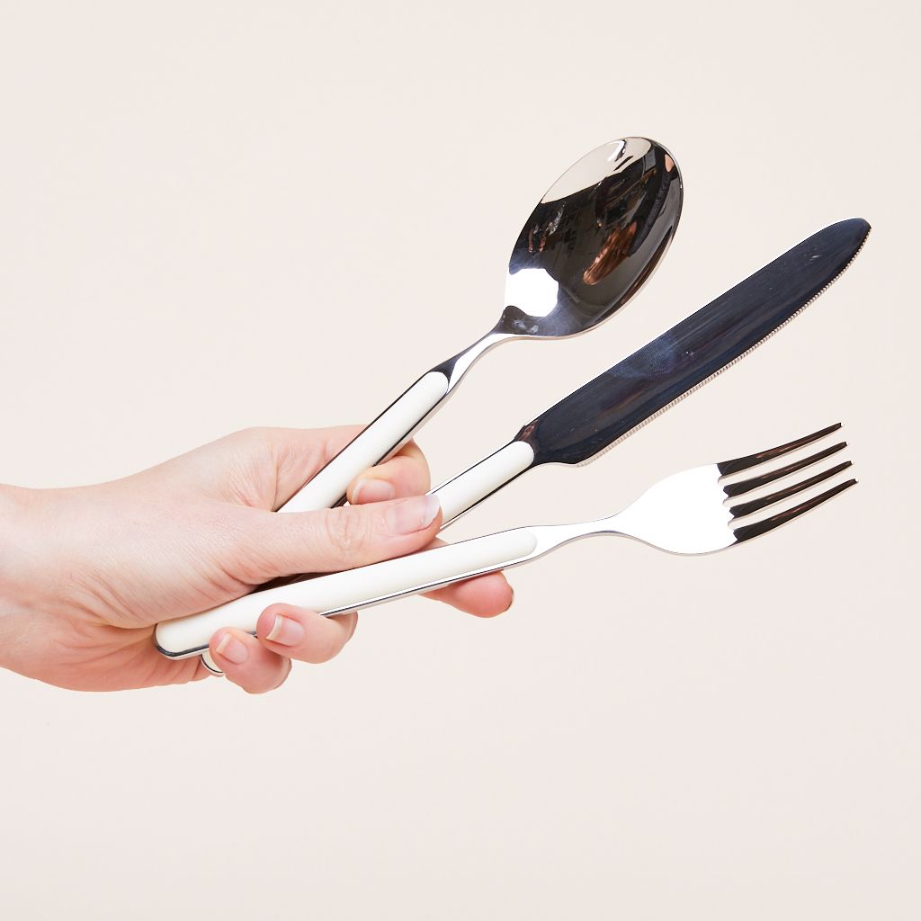 A spoon, knife and fork in silver metal with white trim, held in a hand