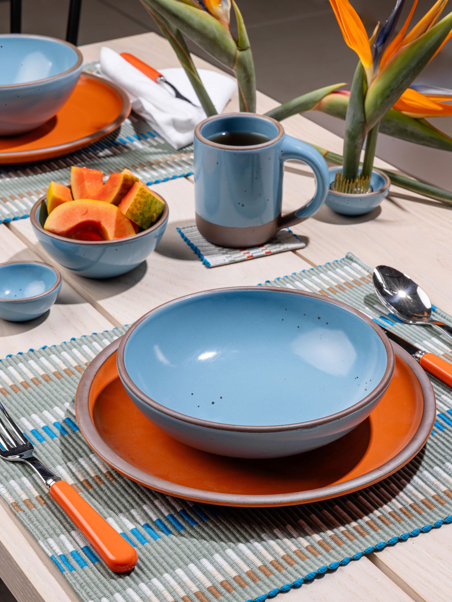 A shallow dinner bowl in a robin's egg blue color sits on a large dinner plate in a bold orange color.
