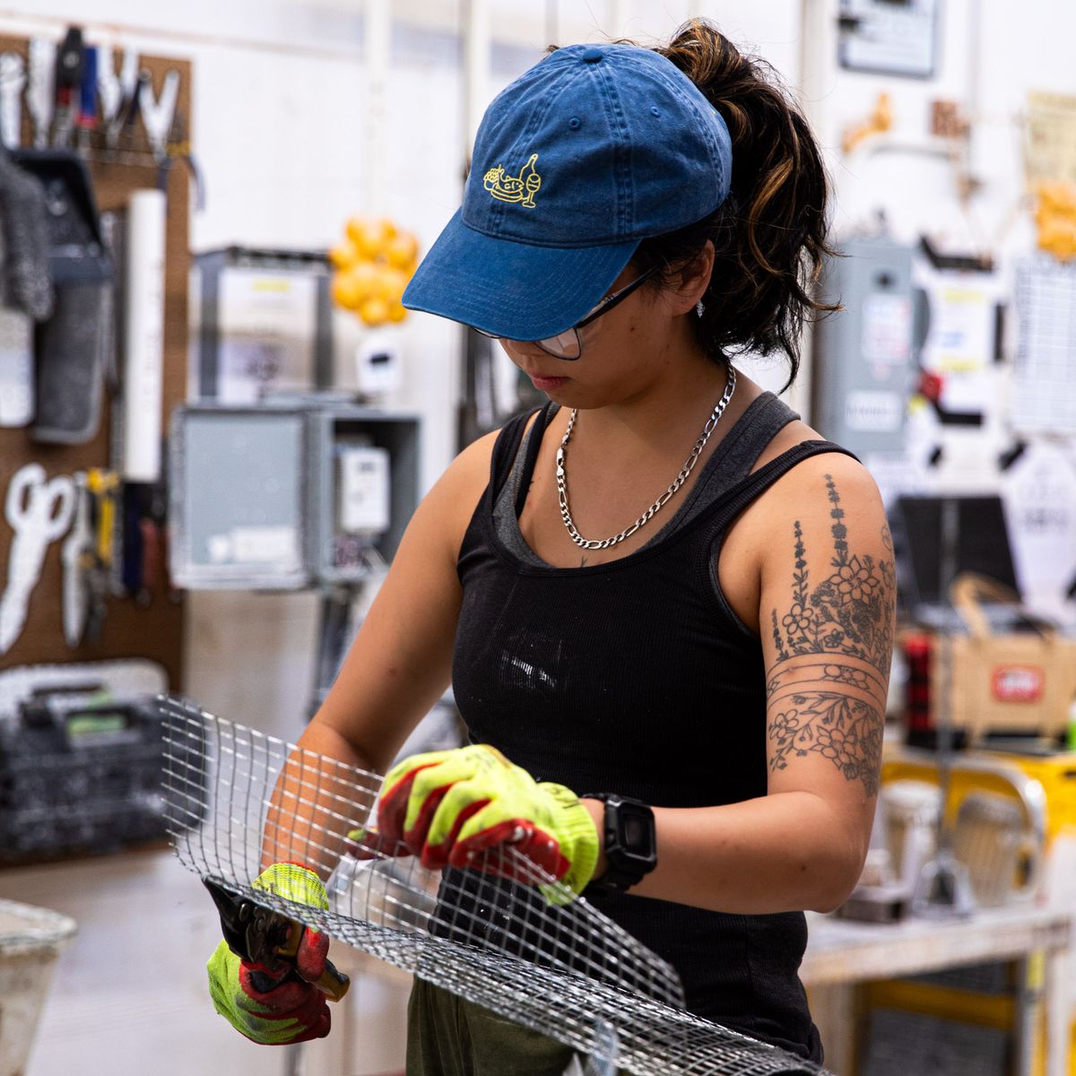 In a manufacturing setting, a person is wearing a classic blue baseball hat with yellow embroidery on the front depicting a feast of fish, fruit and wine.