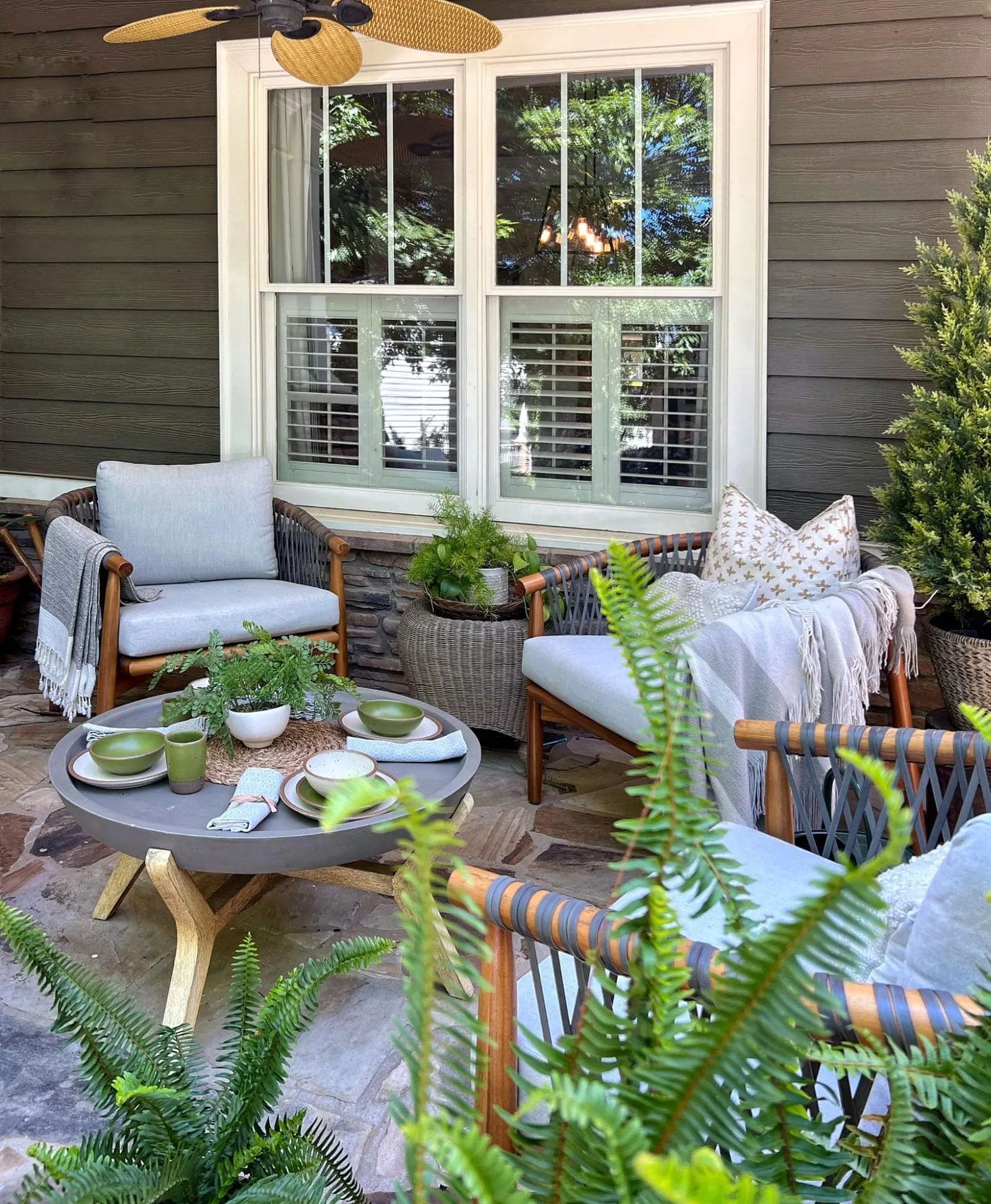 An outdoor seating area dressed up for spring: with Fiddlehead pottery, fiddlehead ferns, and cozy blankets thrown on patio furniture.
