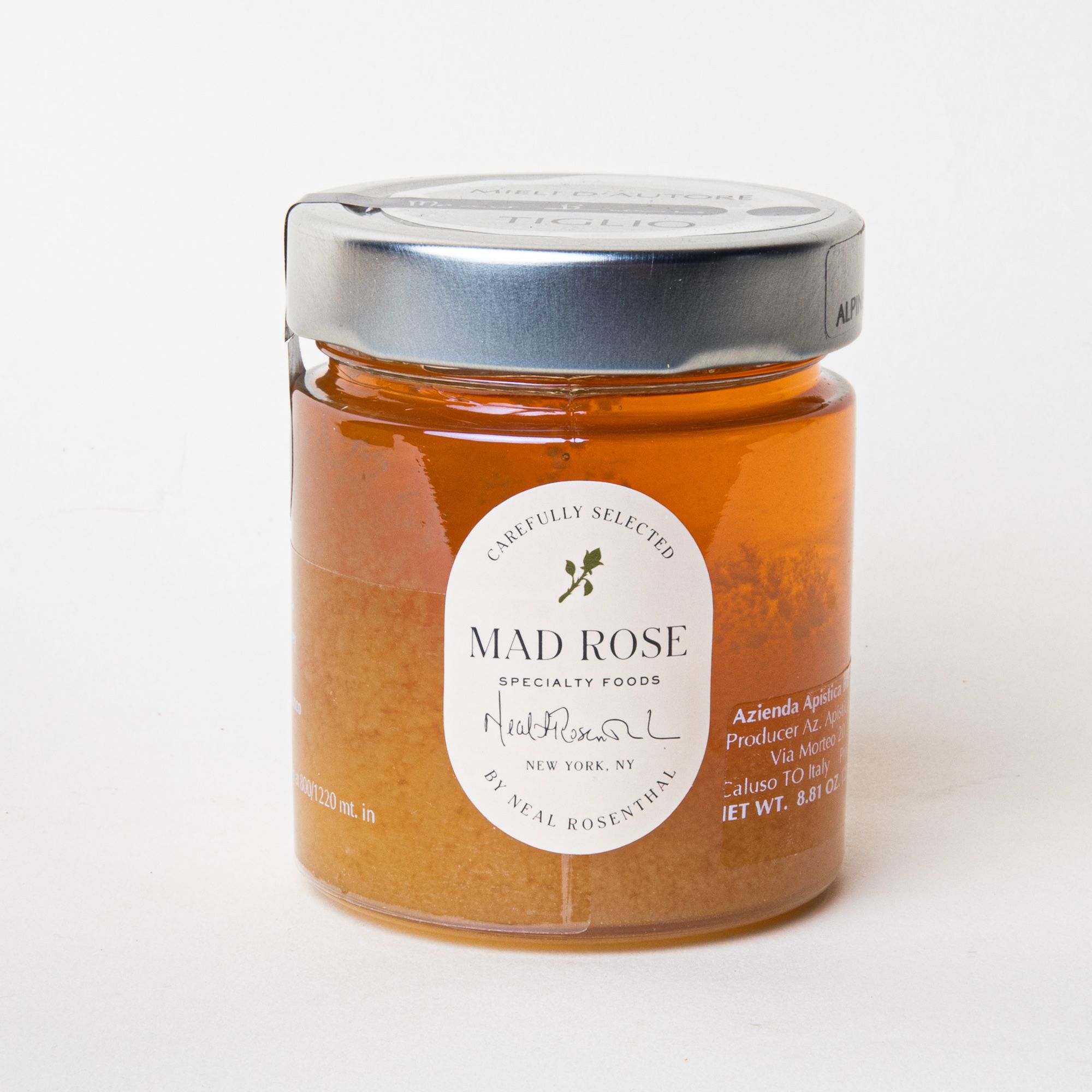 Short clear jar filled with honey and topped with a metal screw cap and small white label