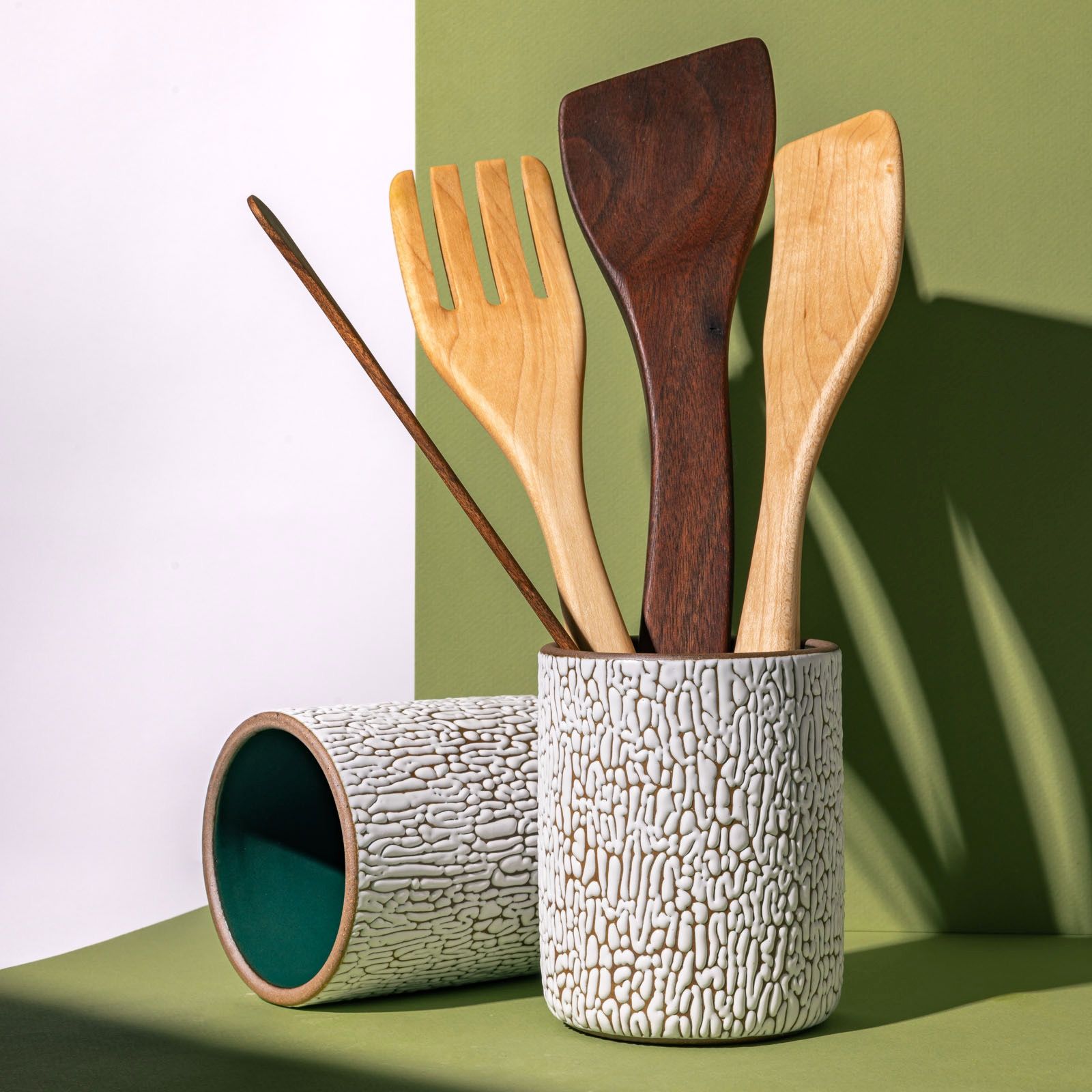 Two big white ceramic vessel with cracked texture and the interior being dark teal filled with wooden utensils