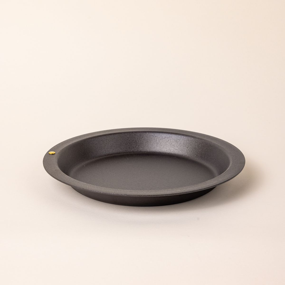 A simple iron pie plate with a wide rim and shallow body