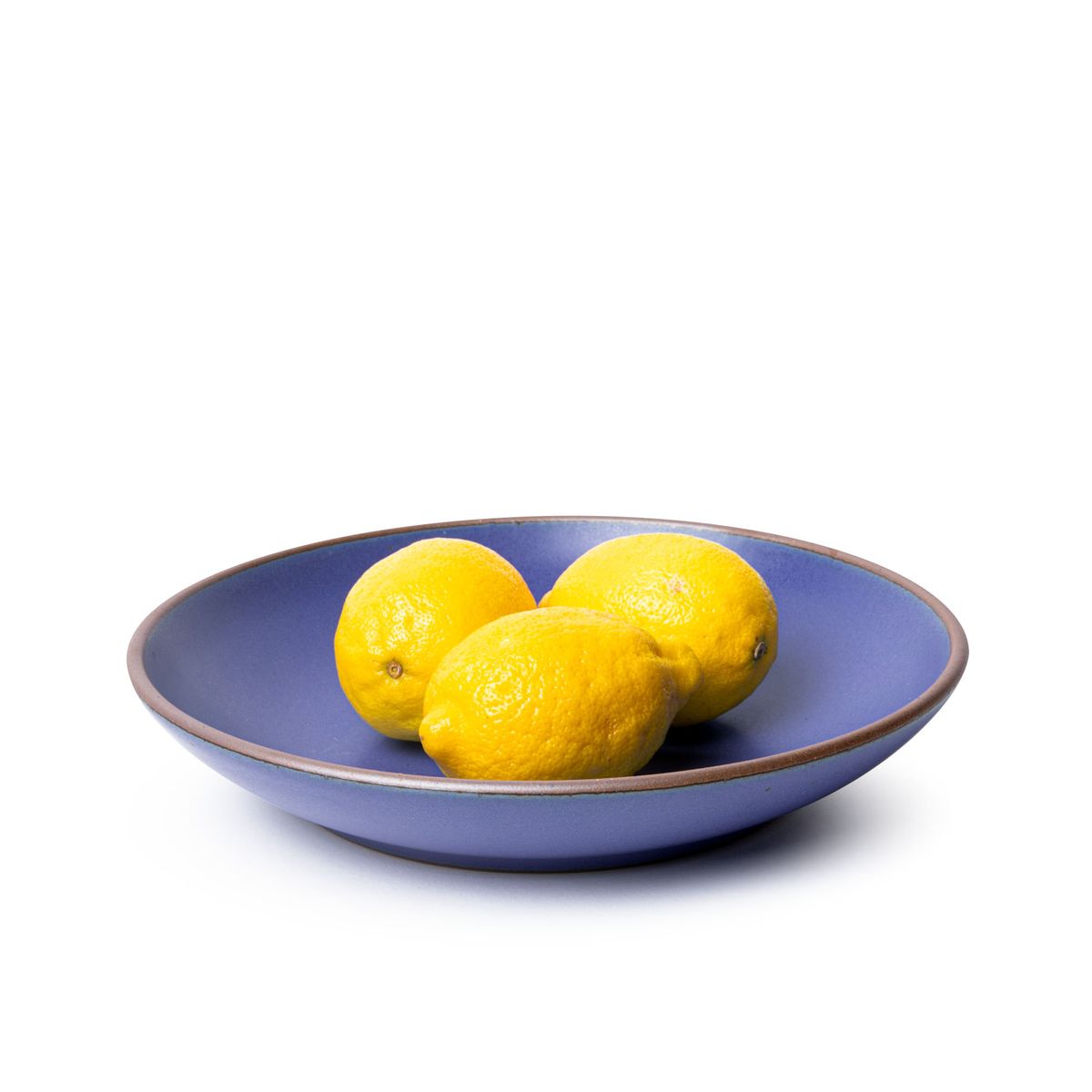 Three whole lemons on a large ceramic plate with a curved bowl edge in a true cool blue color featuring iron speckles and an unglazed rim.