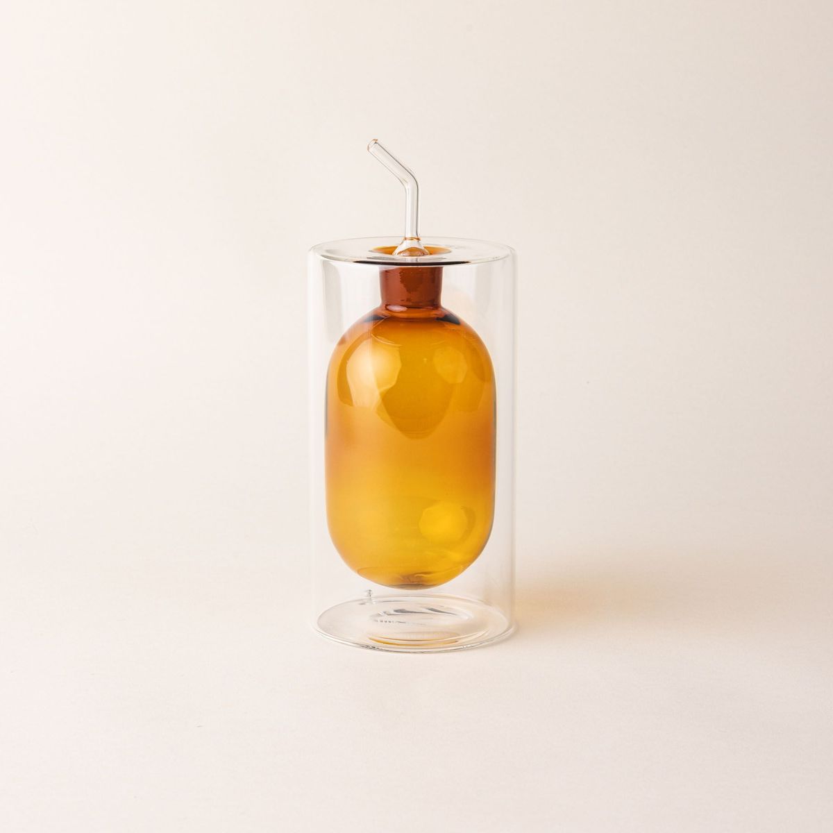 An artful glass cruets in a an orange color. There is a rounded bulb that acts as a container for the cruet, surrounded by a doubled glass wall.