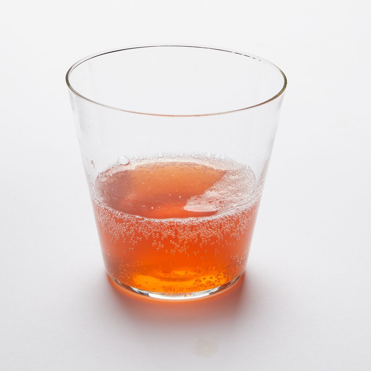 A short drinking glass made of clear glass, filled with amber drink
