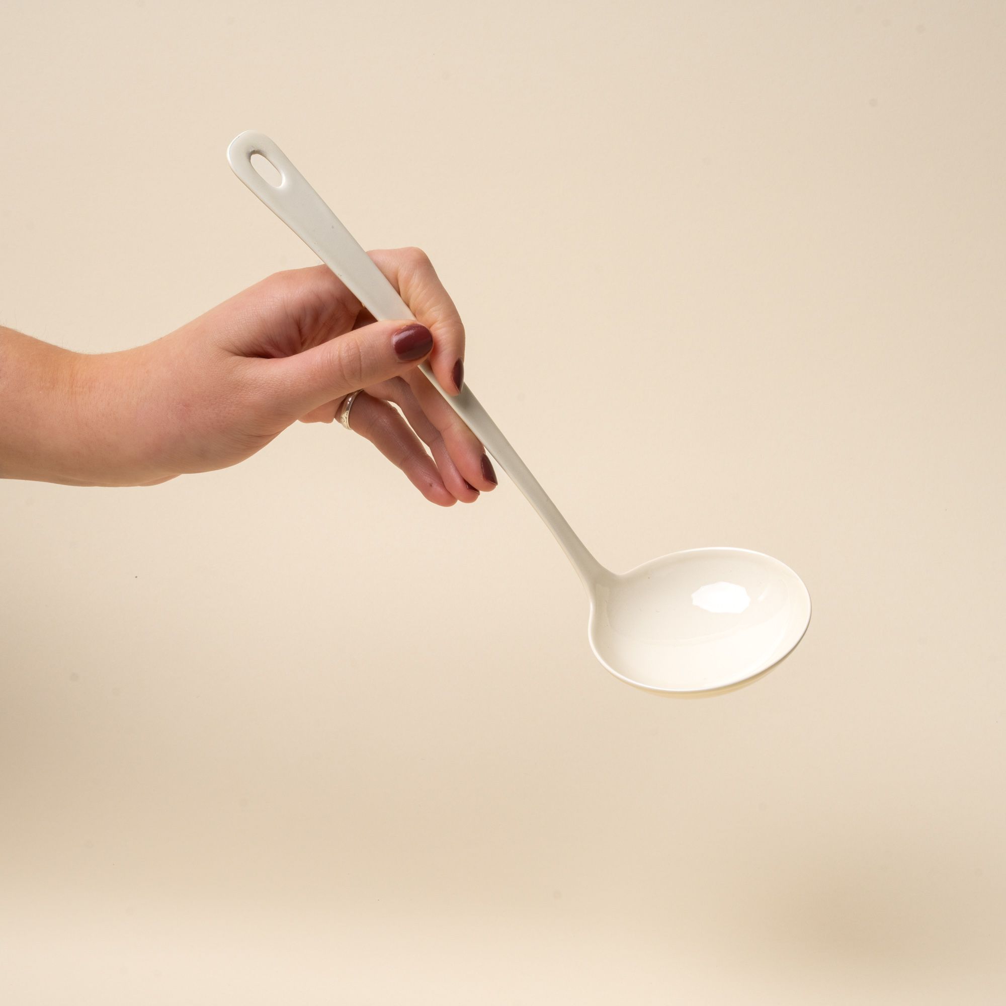A hand holds a white enamel ladle with a hole at the end of the handle for hanging.