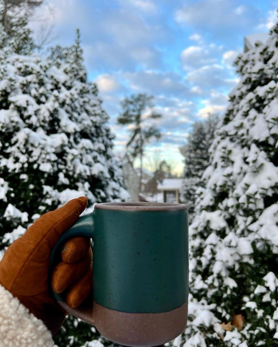 Where WON'T you take your Mug? A gloved hand holds up an East Fork Mug against a backdrop of snow covered evergreen trees.