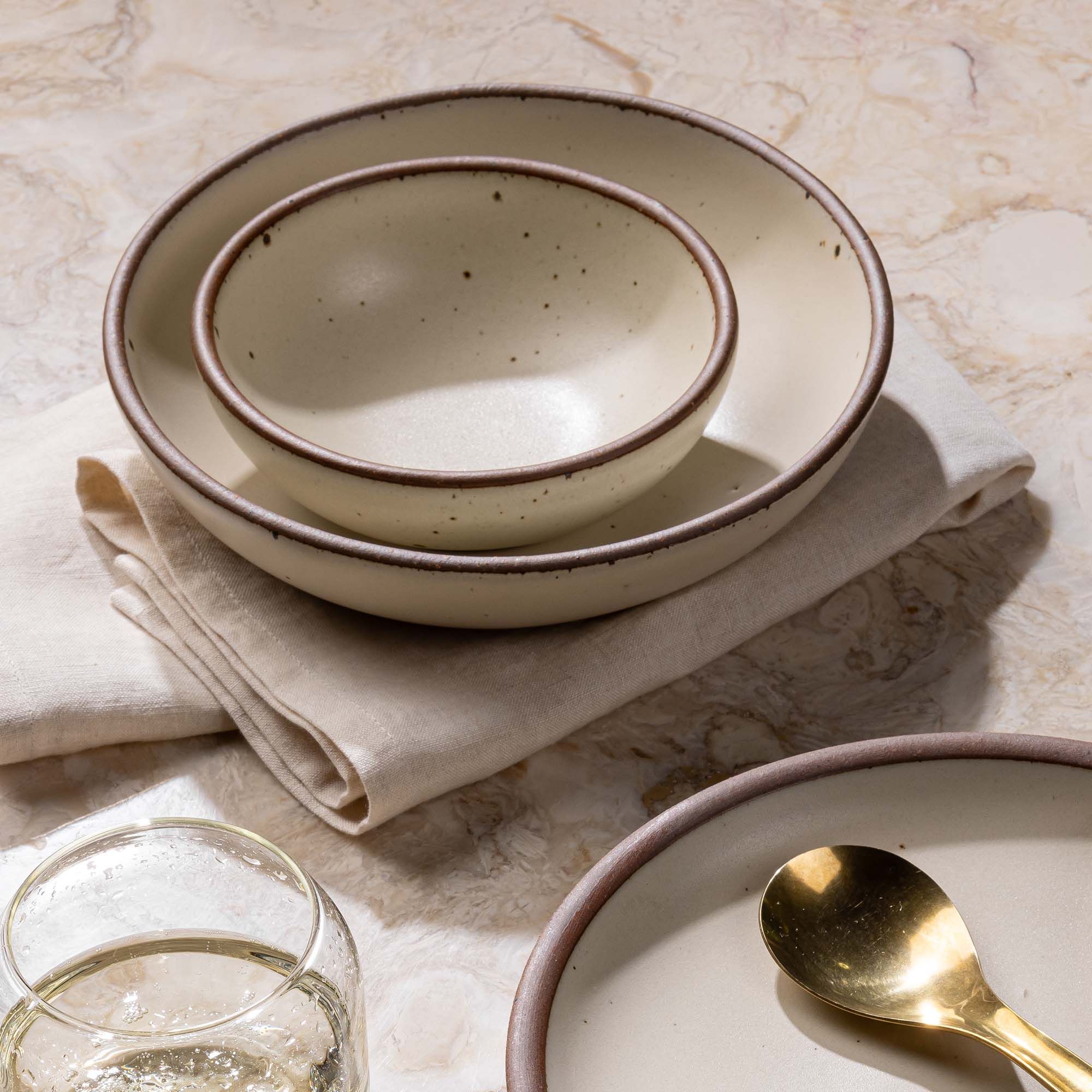 Two nesting ceramic shallow bowls in an off-white cream color with a napkin in the same color.