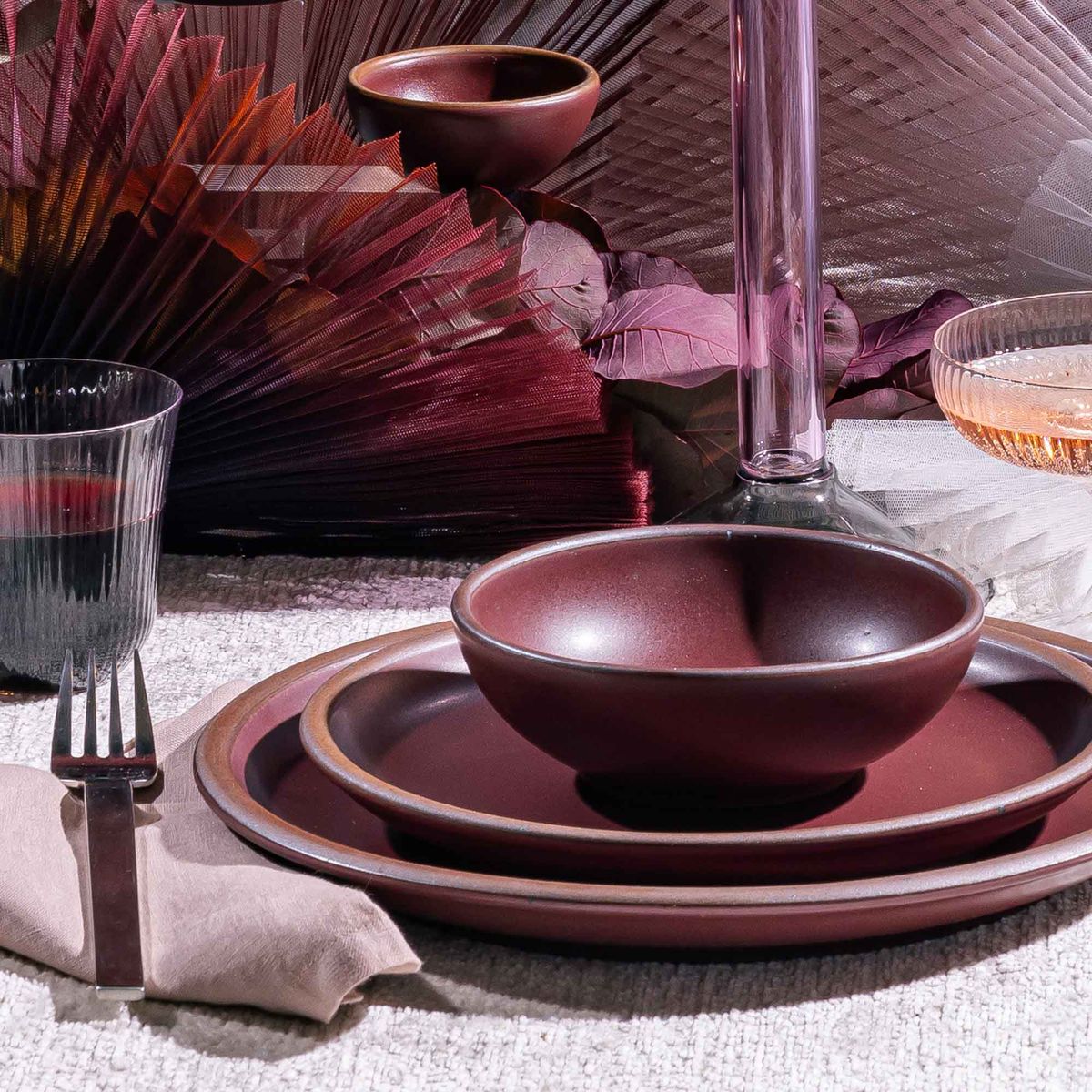 A place setting with plum dinner plates and a shallow bowl with a glass of wine and silverware