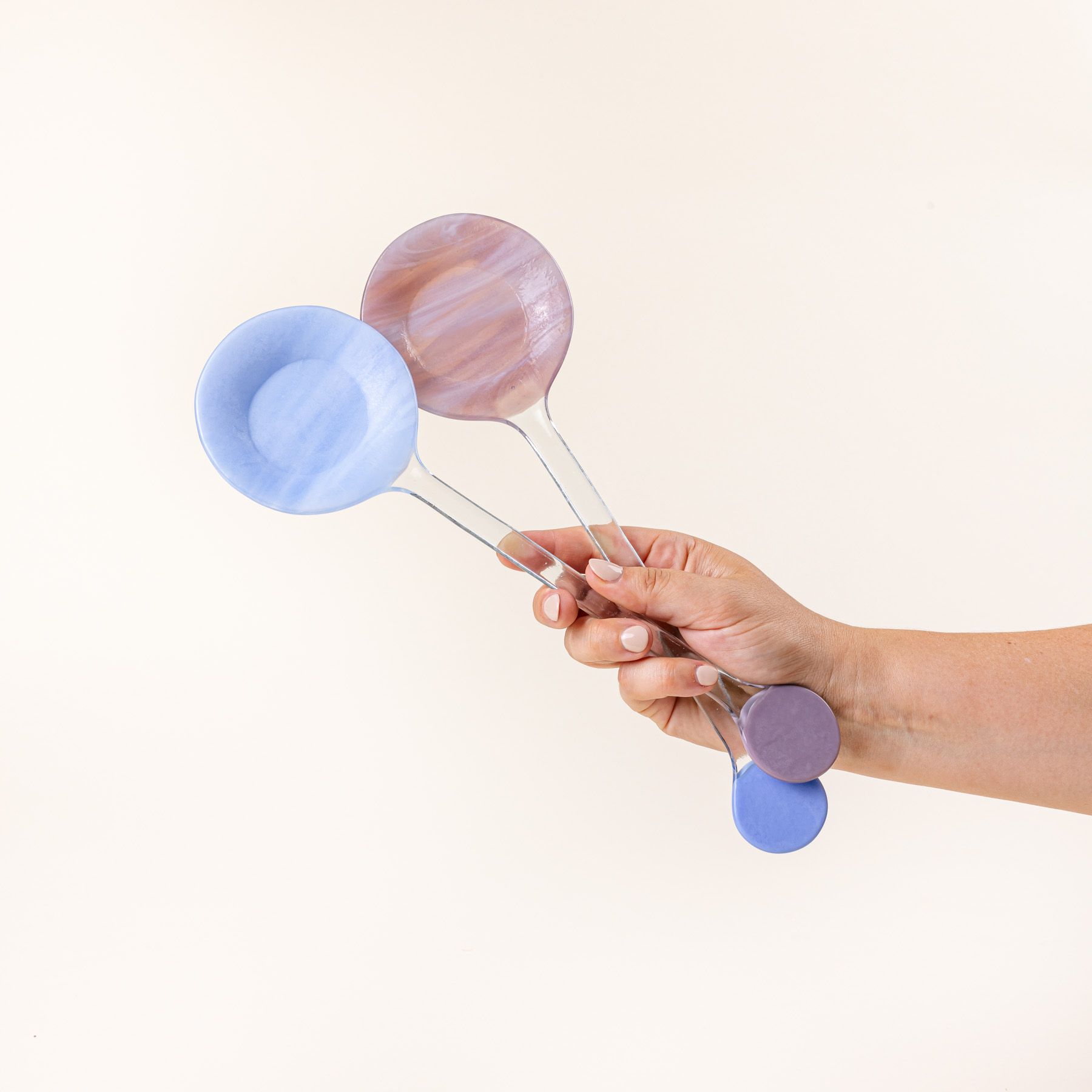 A hand holds  modern glass colorblocked serving spoons in periwinkle and plum colors.