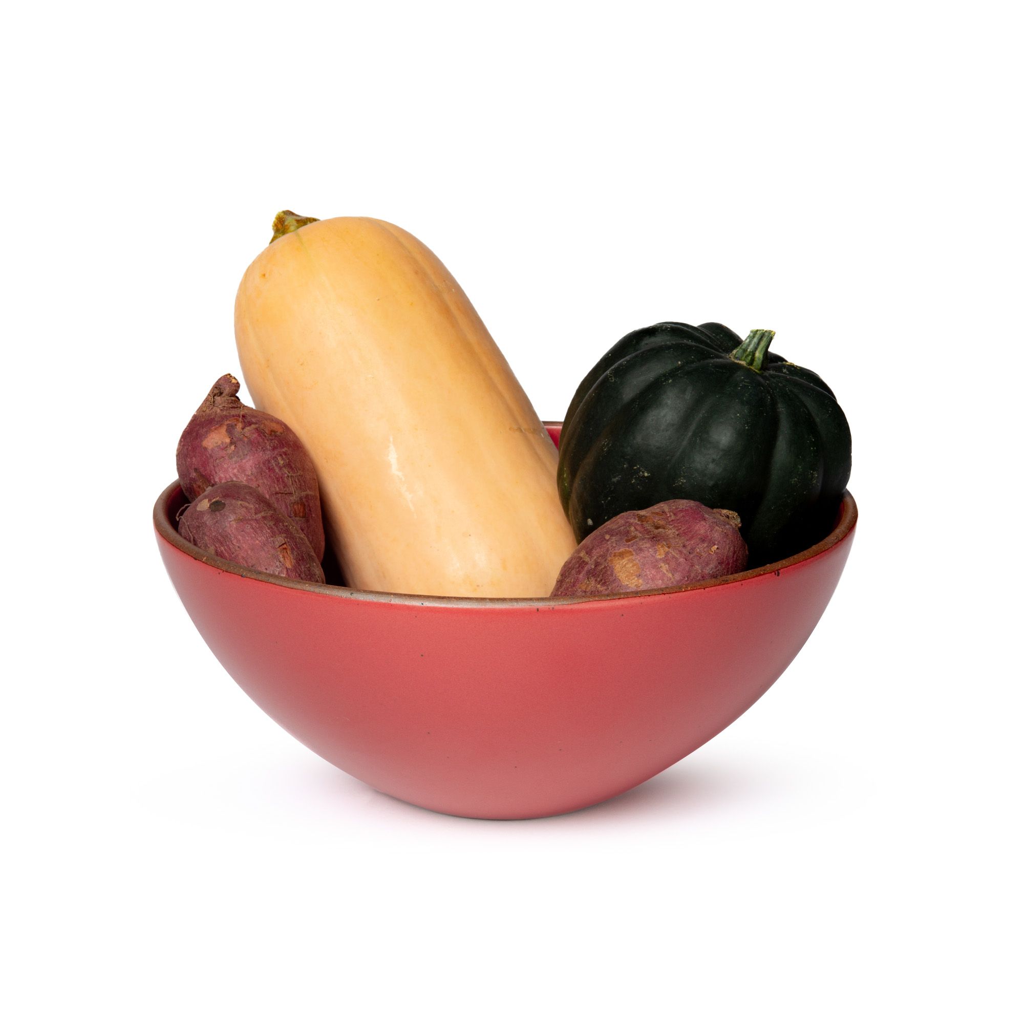 A large ceramic mixing bowl in a bold red color featuring iron speckles and an unglazed rim, filled with sweet potatoes and gourds.