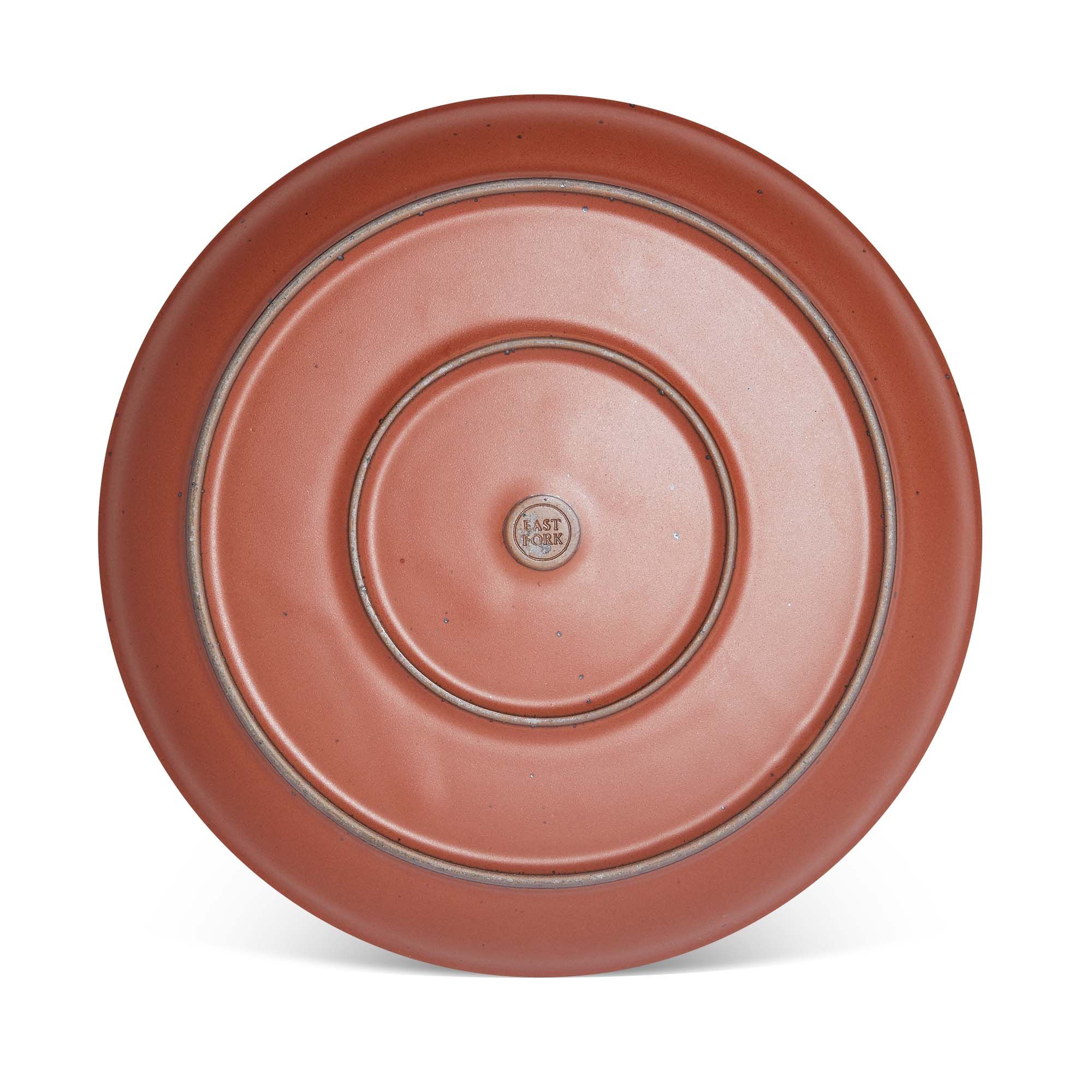 Bottom of a large ceramic platter in a cool burnt terracotta color featuring iron speckles and an unglazed rim
