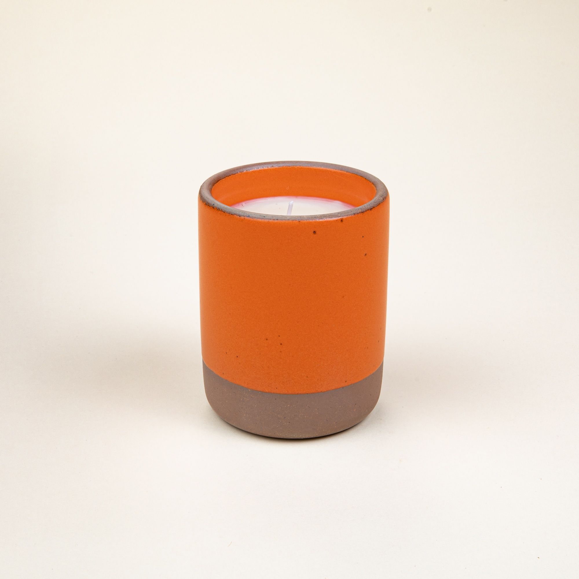 Small ceramic vessel in a bold orange color with candle inside.