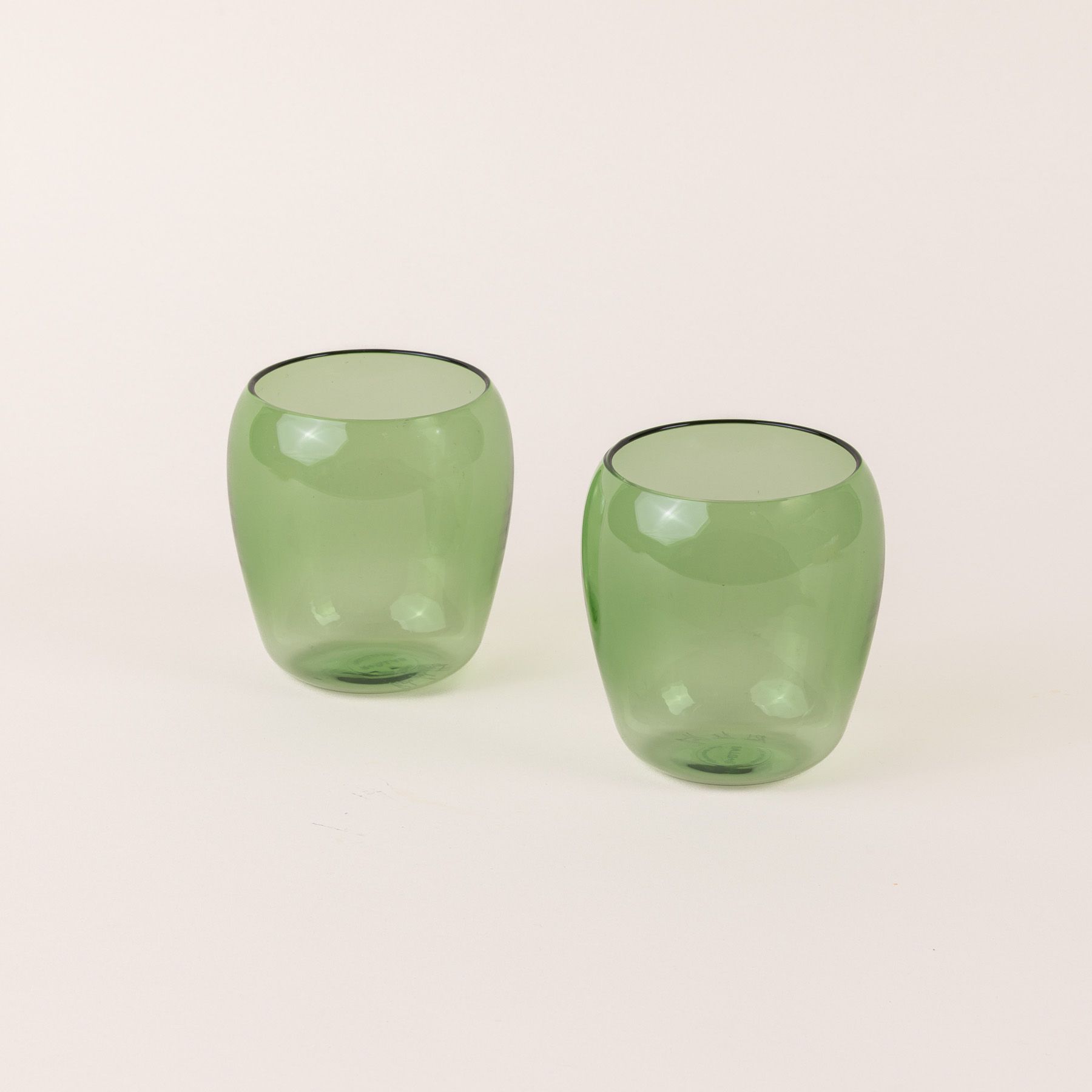 Two short light green glass tumblers with a slight curve inward on the top.