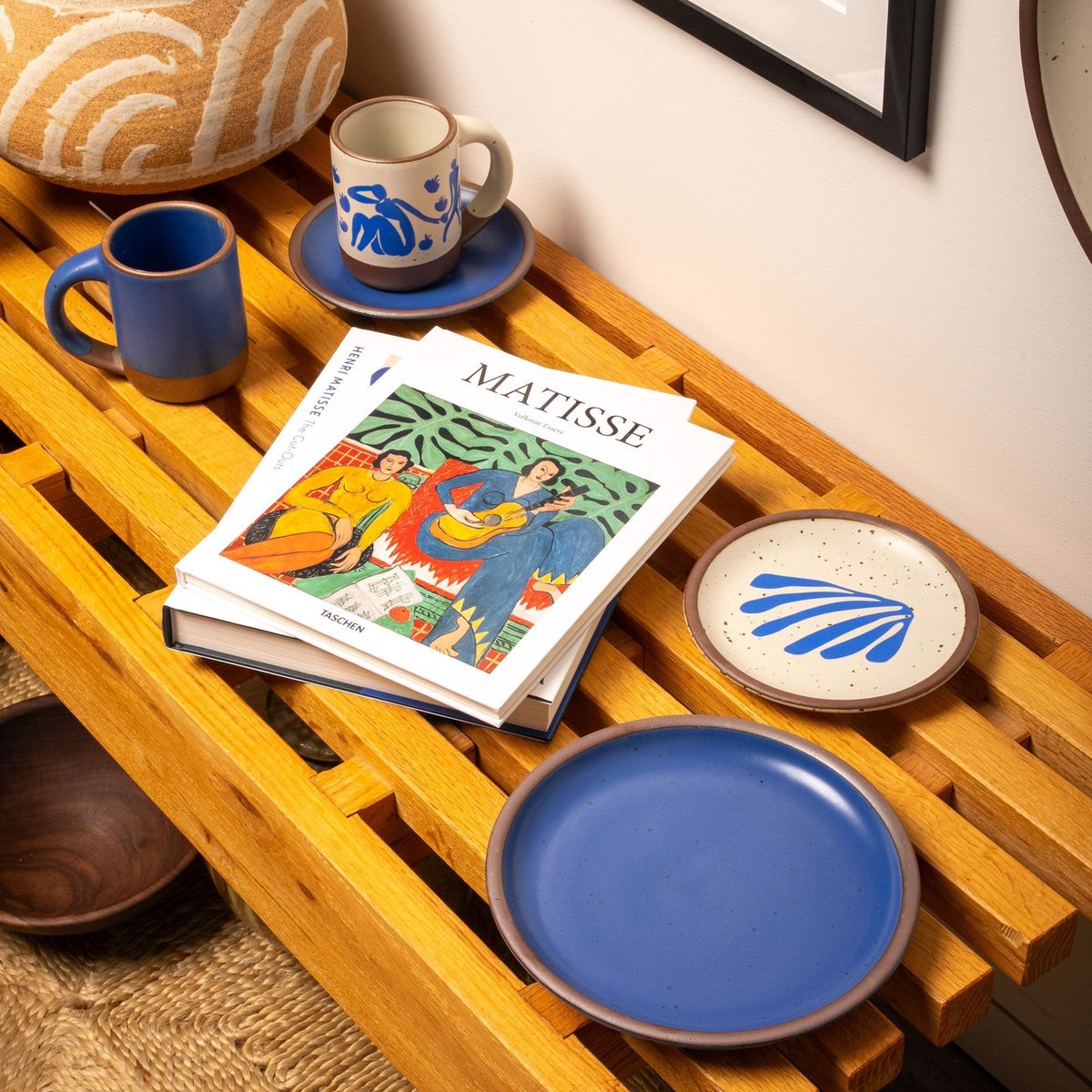 Pieces from The Matisse Collection - some plates and mugs - are displayed on a wooden bench with a book about Henri Matisse.