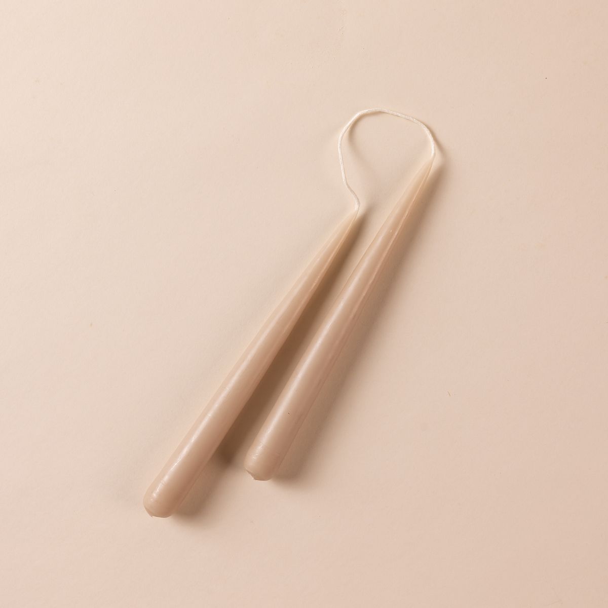A pairs of taupe taper candles with the wick connected at the top.