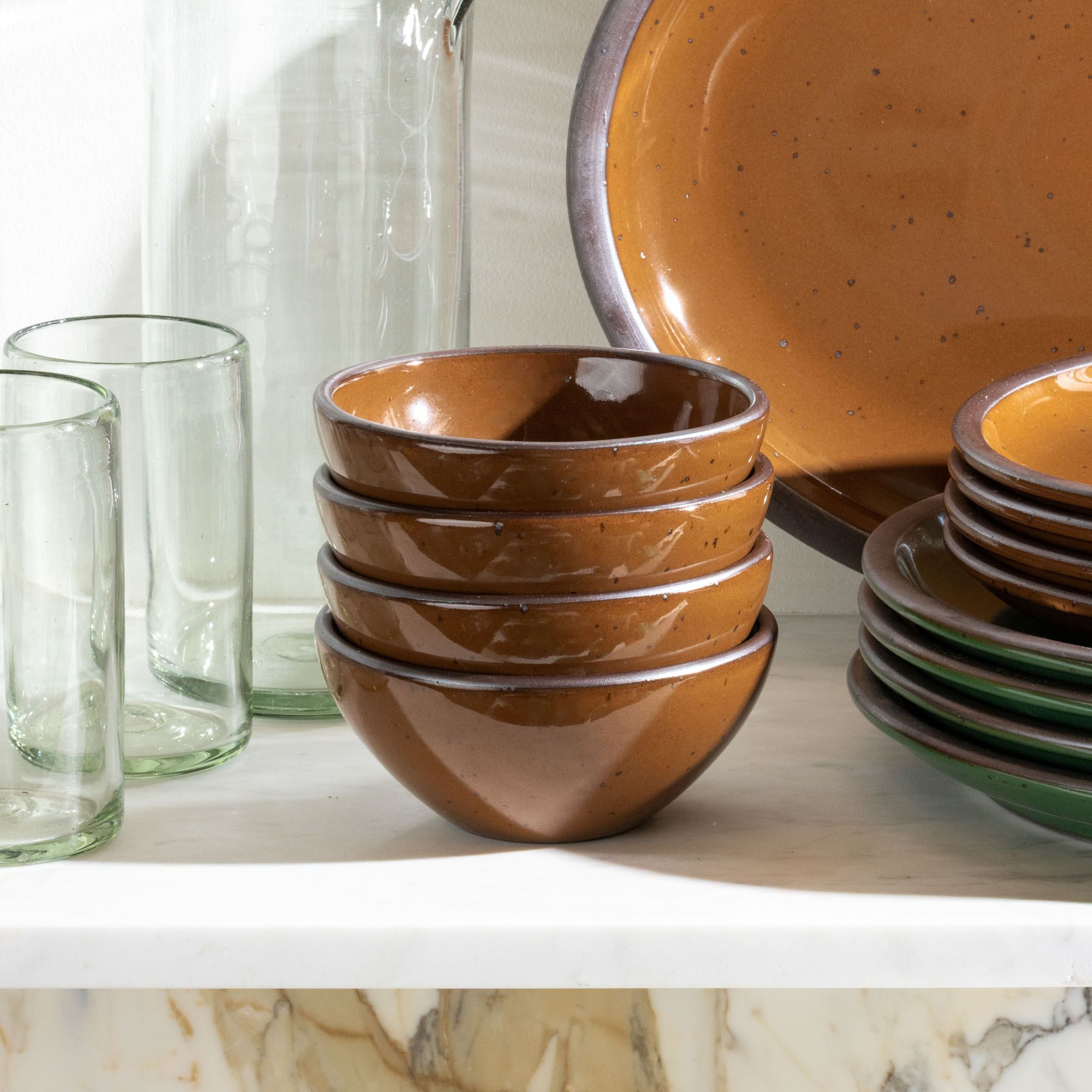 A stack of 4 small dessert sized ceramic bowls in a glossy caramel brown color on a white shelf