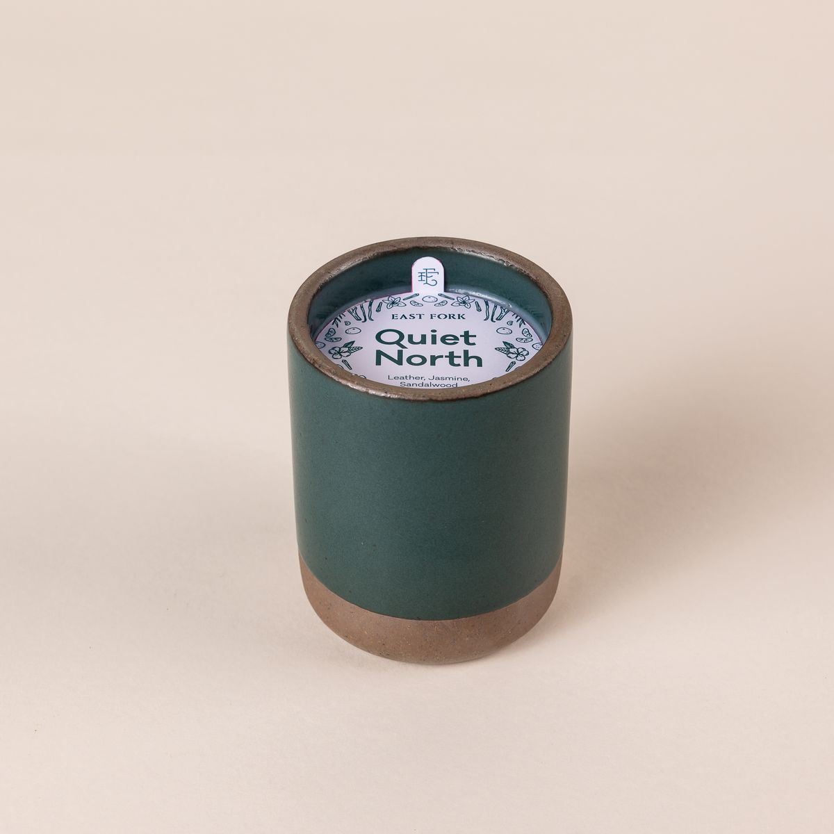 Large ceramic vessel in a deep dark teal color with candle inside. On top is a packaging label sitting on top that reads "Quiet North"