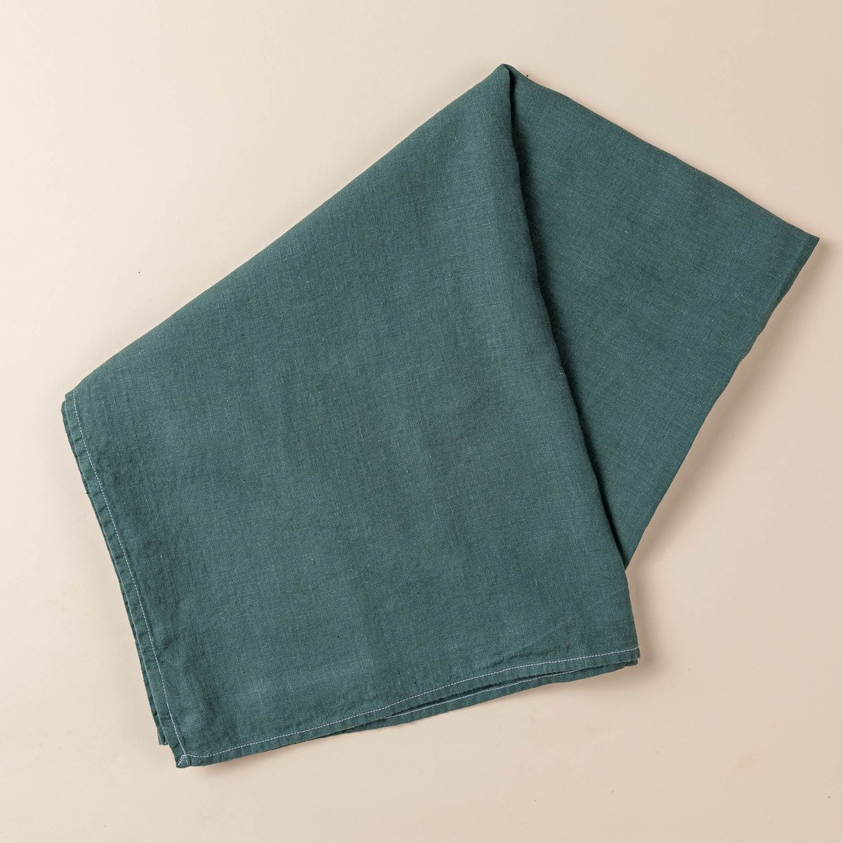 A folded linen tablecloth in a solid deep teal color