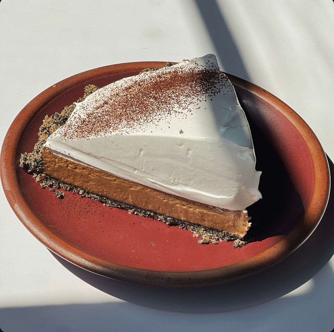 A slice of Yuzu Espresso Meringue Pie on a deep berry color ceramic plate.