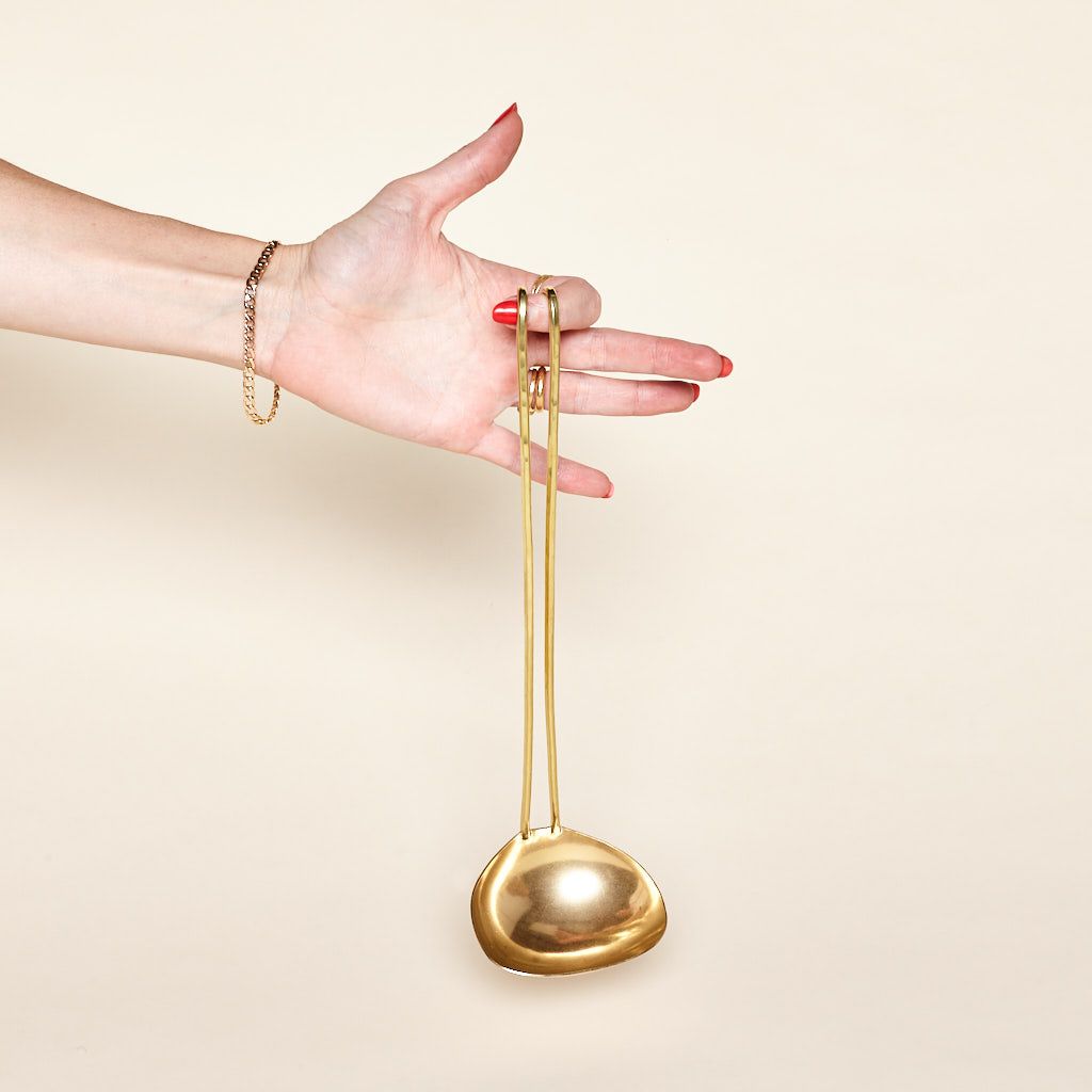 From an index finger, a long brass ladle dangles