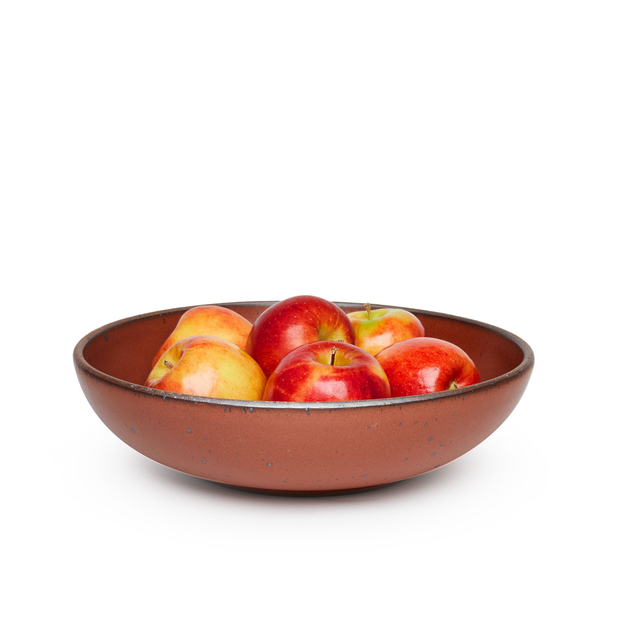 A large shallow serving ceramic bowl in a cool burnt terracotta color featuring iron speckles and an unglazed rim, filled with apples