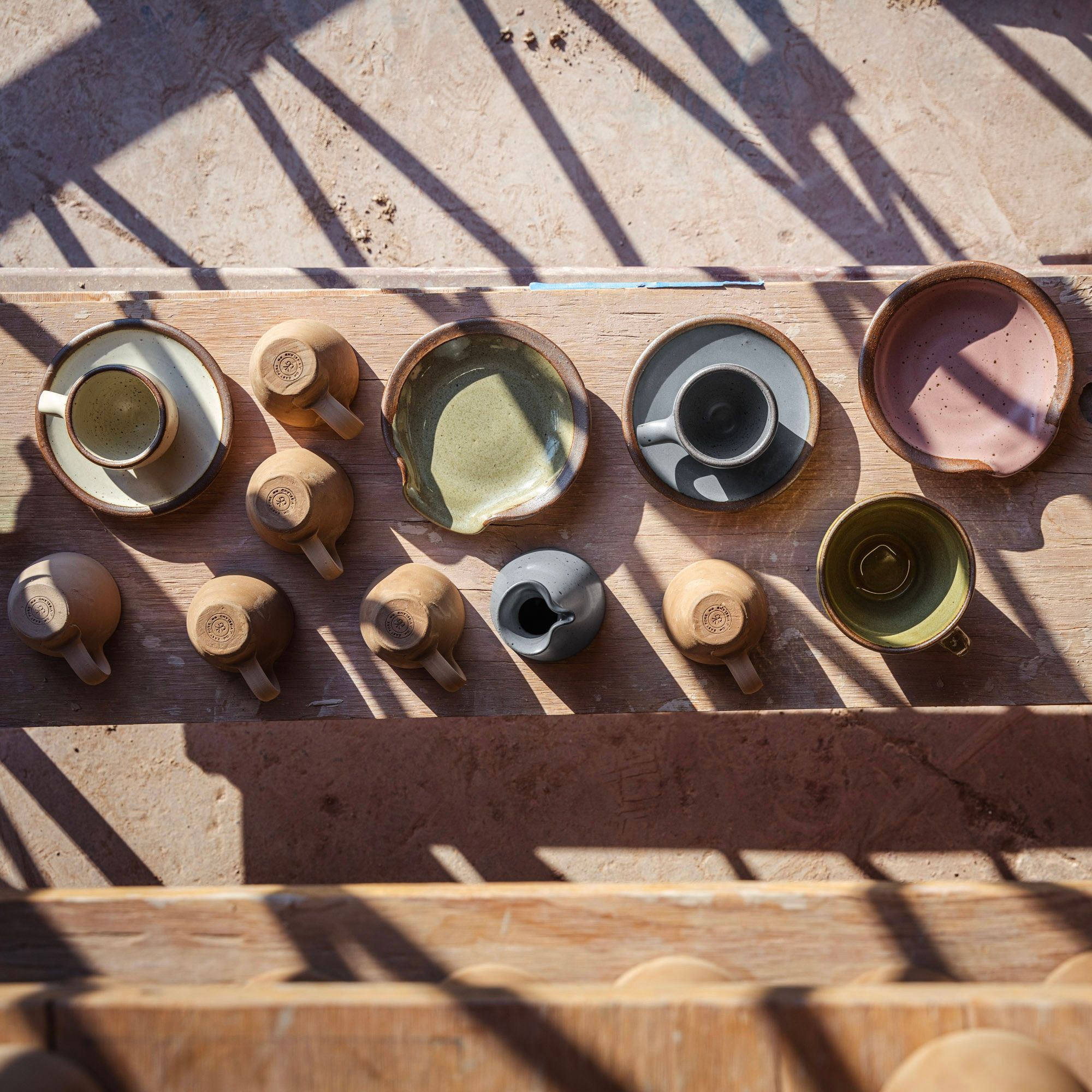 An overhead view of finished workshop pieces, including Spoon Rests, Espresso Cups, and Sunday Morning Mugs, along with bisqueware.