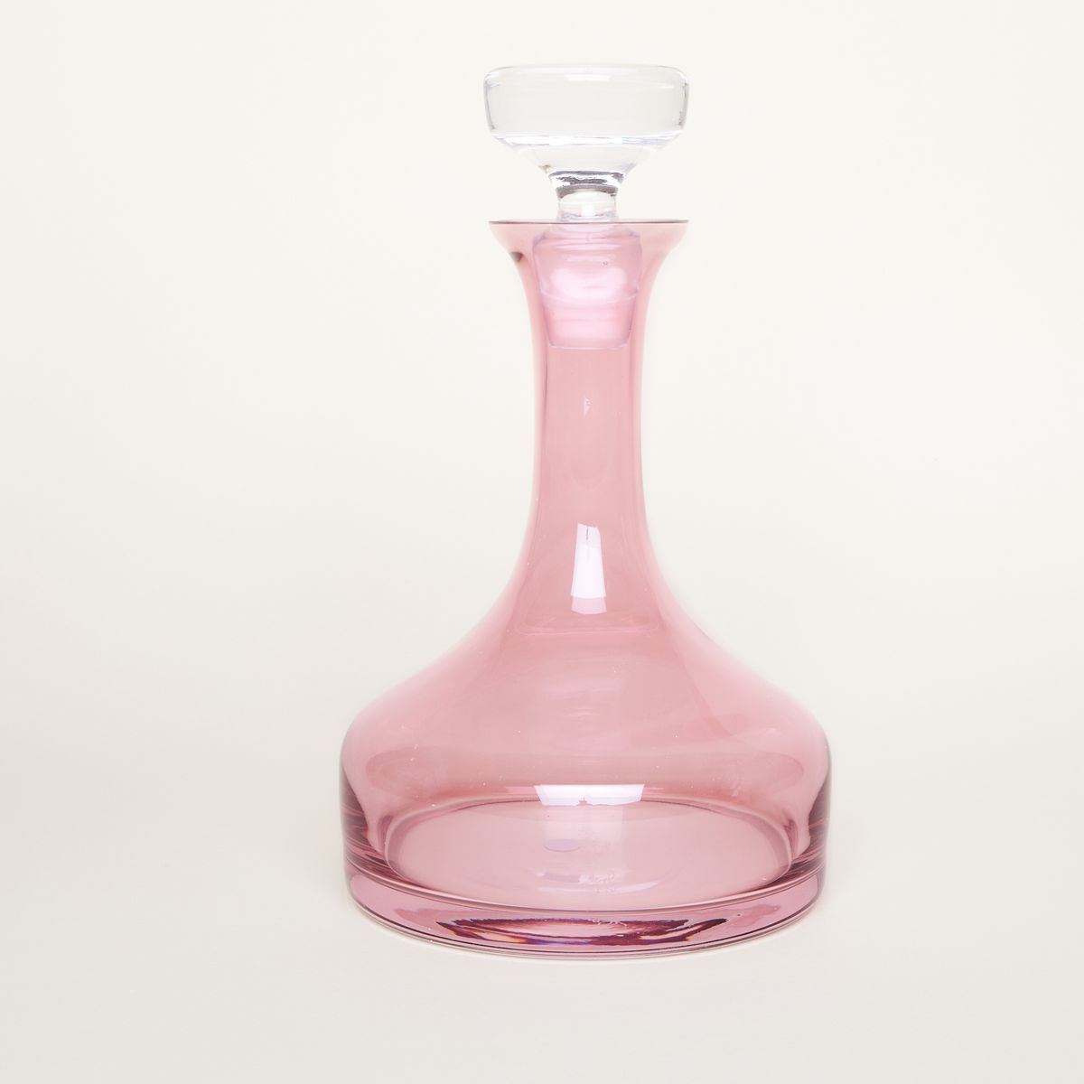A clear glass topper on a pink decanter with a long neck and rounded base.