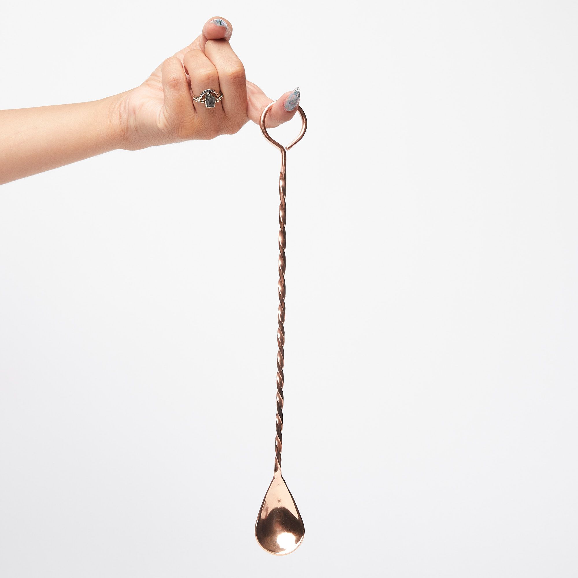 A hand with finger extended hilding long copper cocktail spoon with a twisted handle