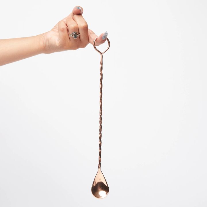 A hand with finger extended hilding long copper cocktail spoon with a twisted handle