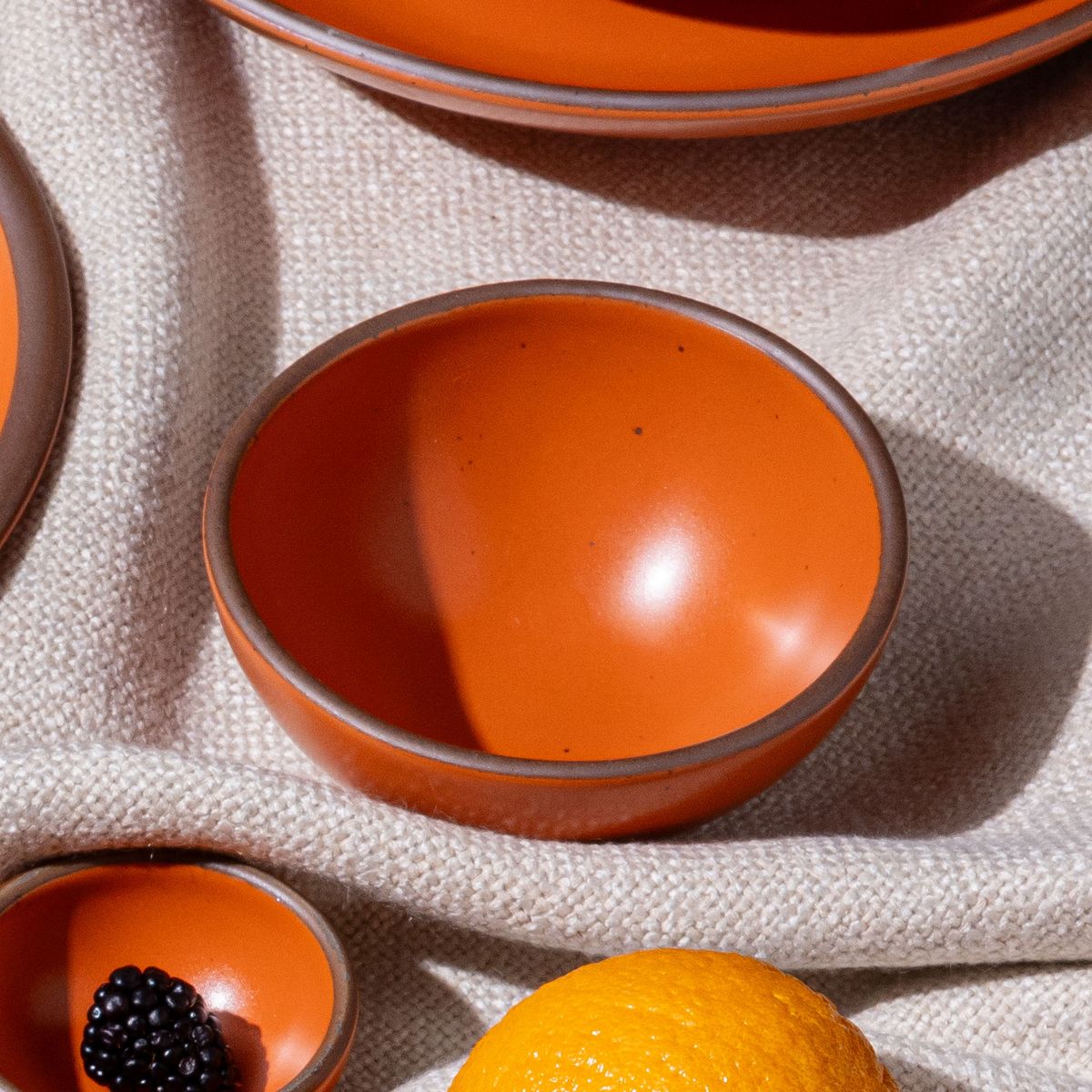 A small dessert sized rounded ceramic bowl in a bold orange color featuring iron speckles and an unglazed rim