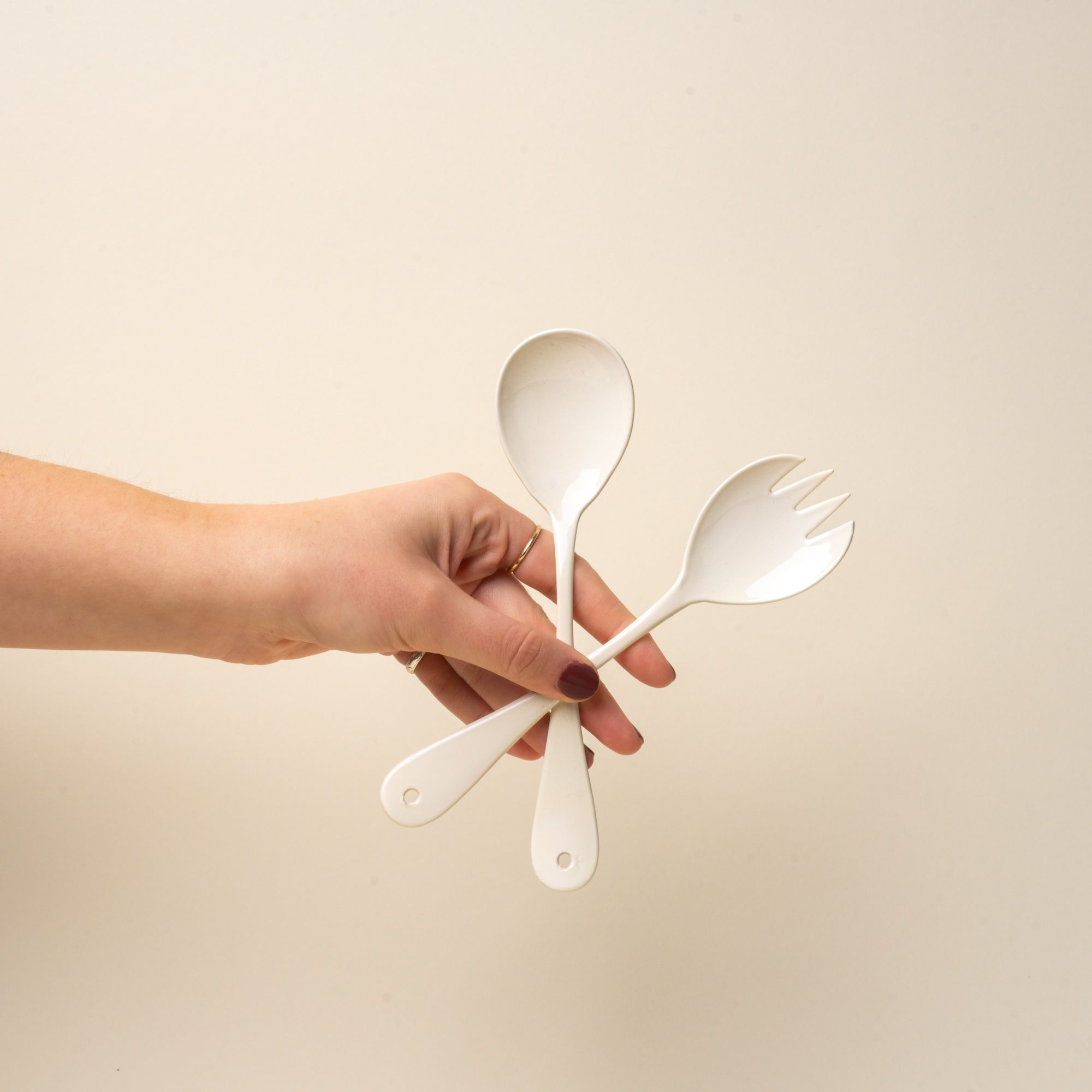 A hand holds a serving fork and spoon set made of white enamel.