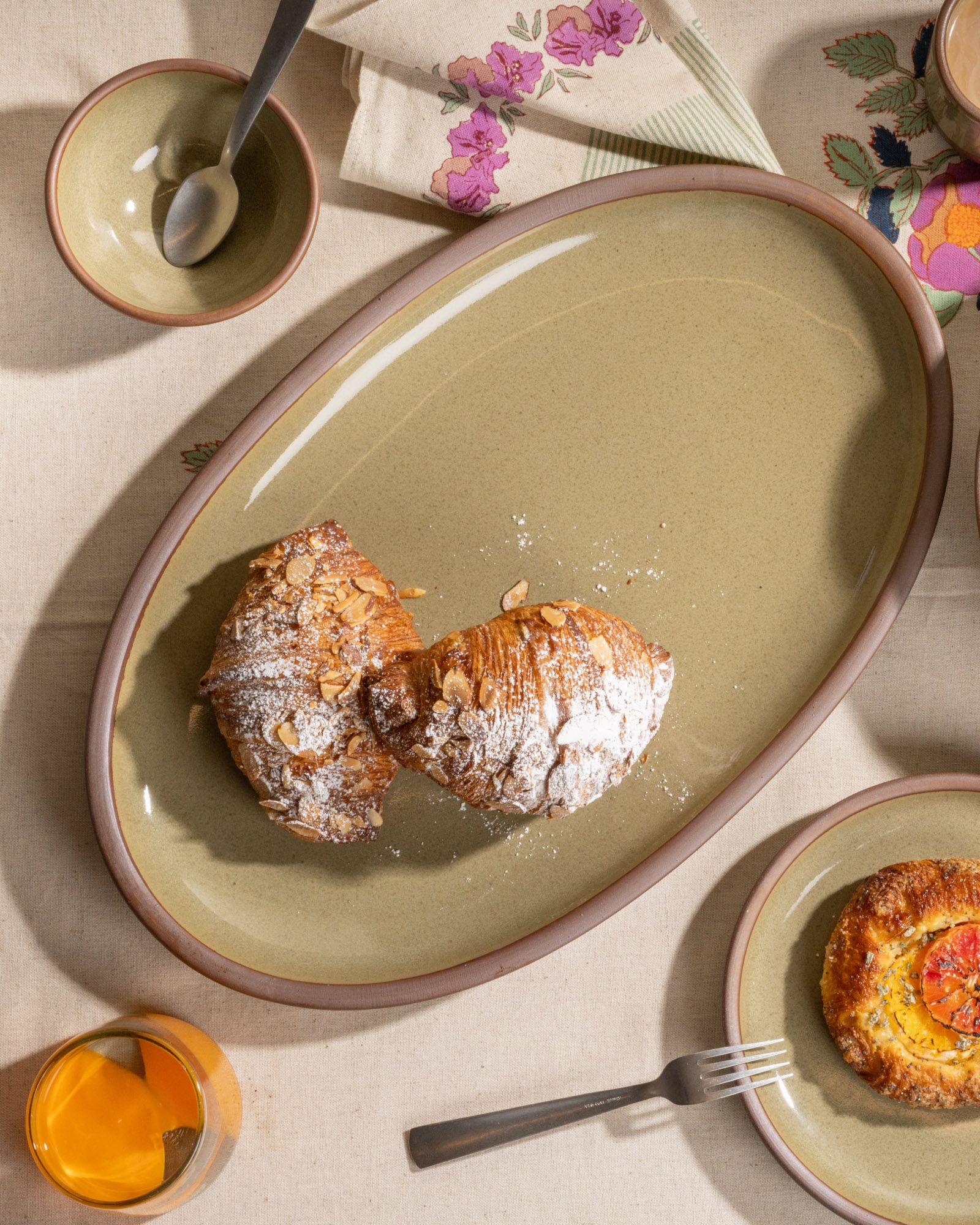 Reflective dappled grey-green oval stoneware platter with almond croissants dusted in powdered sugar.