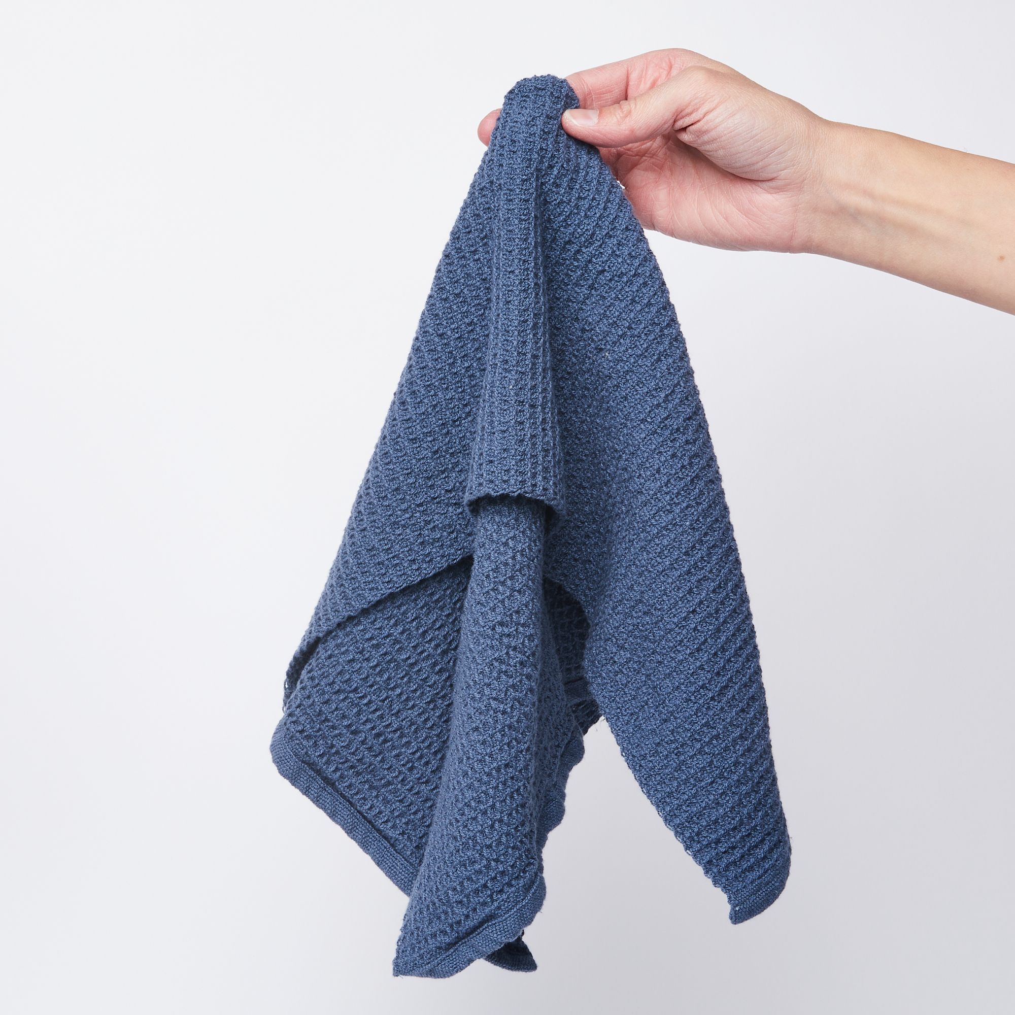 Hand holding a blue waffle weave kitchen towel