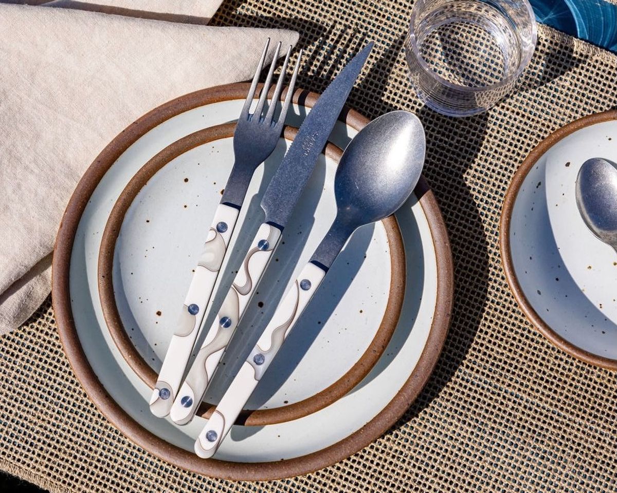 A table setting with a neutral woven placemat, stacked cool white ceramic plates, and ivory marble-handled fork, knife, and spoon.