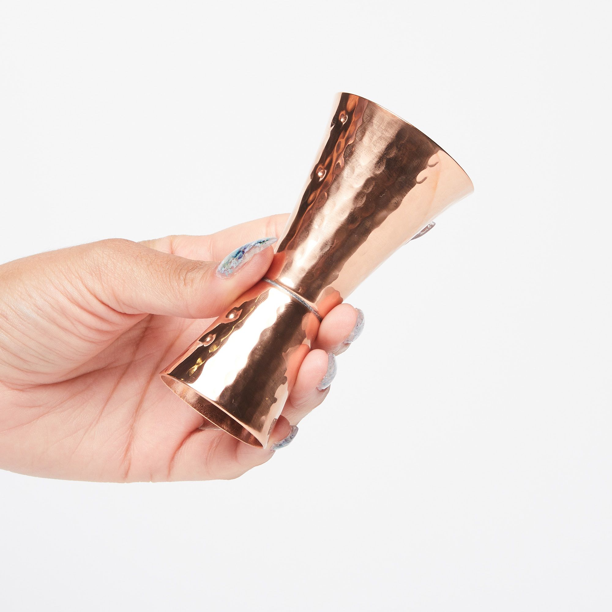 Hand holding a double sided copper shot measurer with the large end up