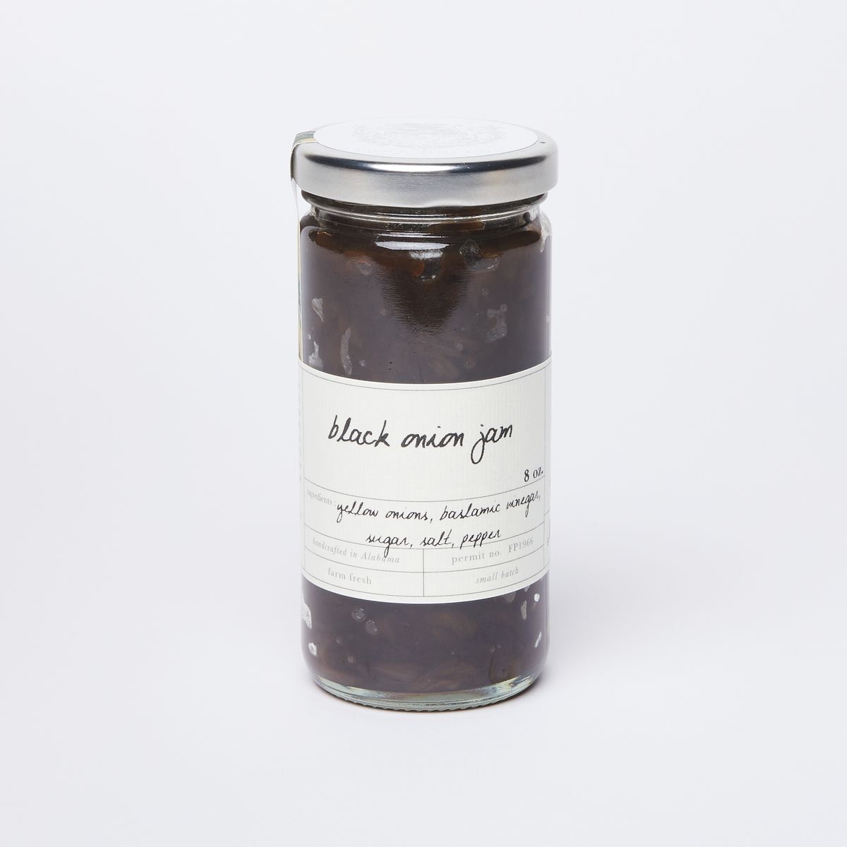 A clear glass jar full of onion jam with a silver lid and a white label that reads "Black Onion Jam"