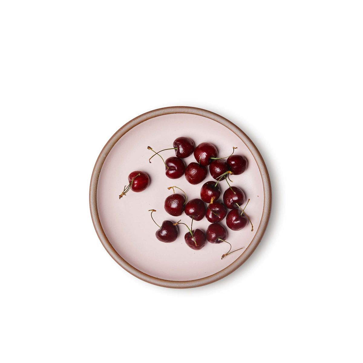 Cherries on a medium sized ceramic plate in a soft light pink color featuring iron speckles and an unglazed rim