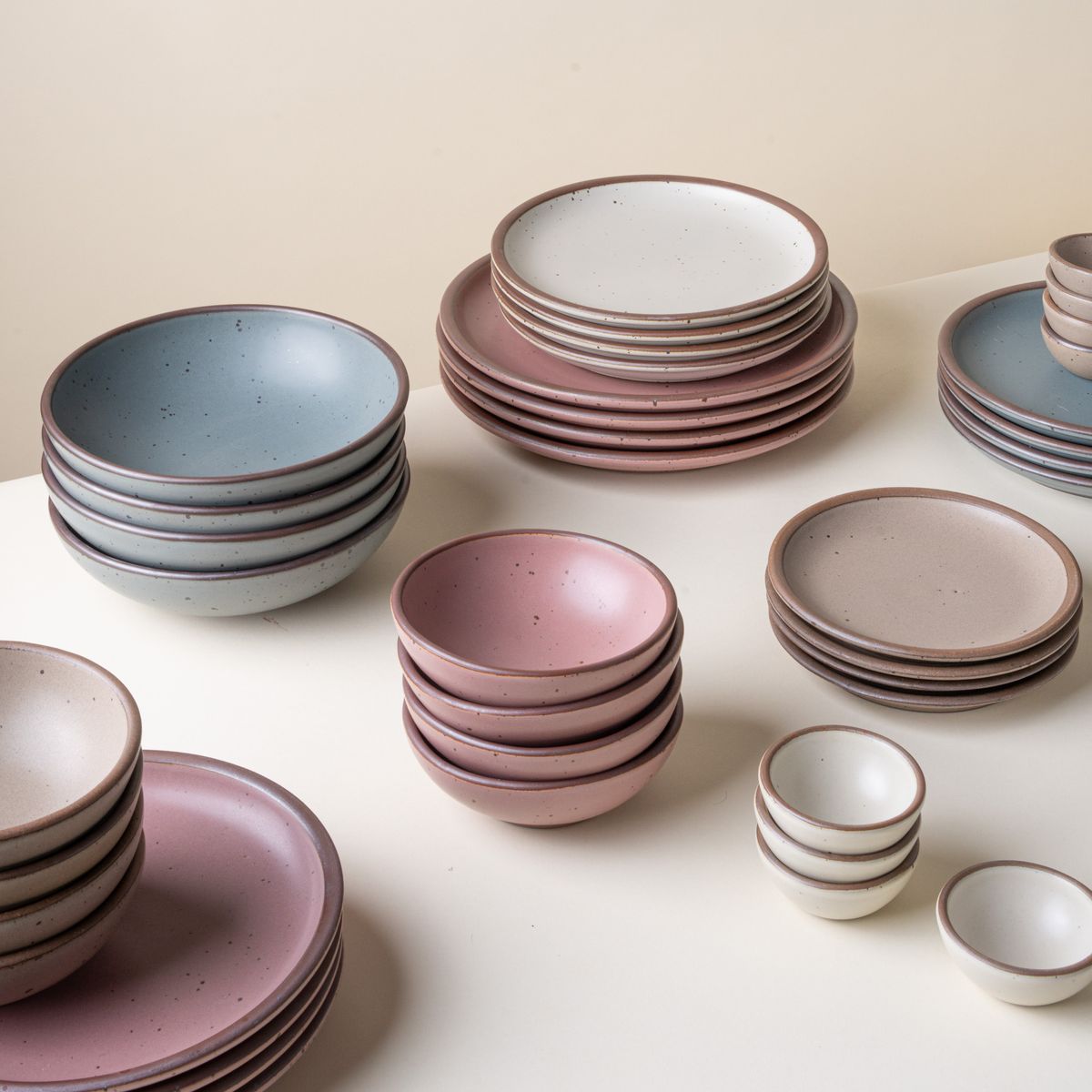 A stack of several plates and bowls in different sizes in sets of 4, in blue-grey, dusty pink, pale brown and off-white colors.