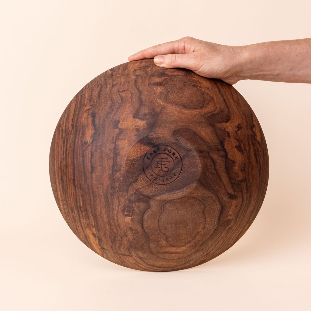 A hand showing off the bottom of a handcrafted wooden walnut bowl that has an engraved stamp on the bottom that reads, "East Fork Pottery".
