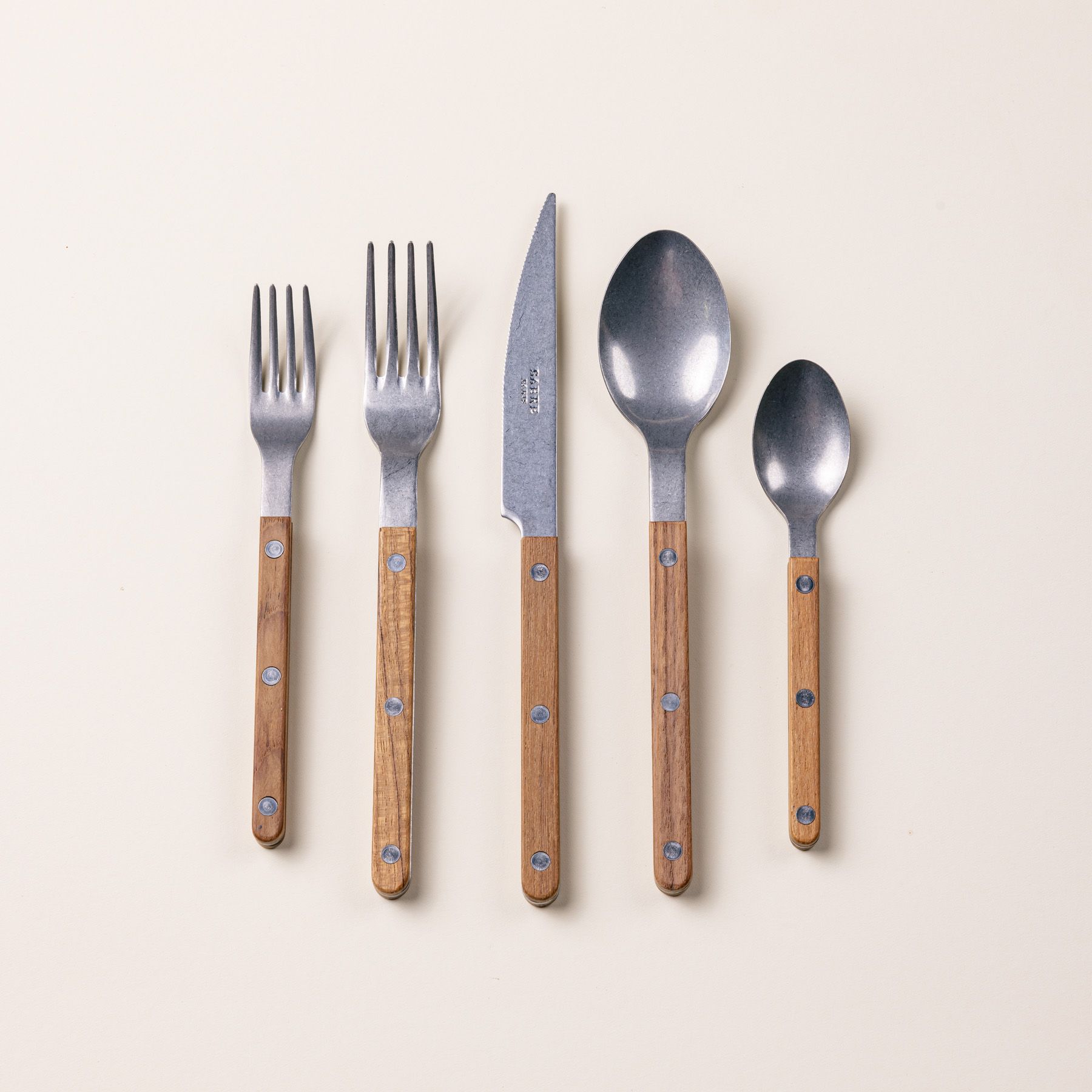 A set of 5 flatware pieces with a teak wood handle: a salad fork, dinner fork, knife, spoon, teaspoon