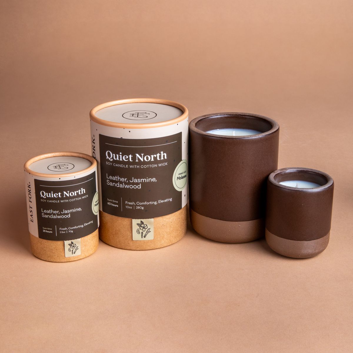 Small and large ceramic vessel next to each other in a dark brown color with candles inside each. Cardboard tube packaging is on the left with branding stickers that say "Quiet North".