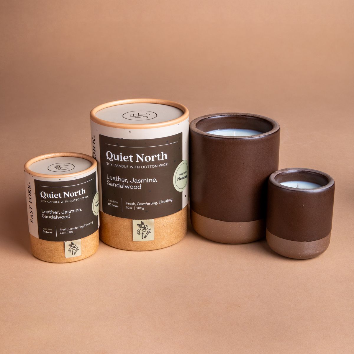 Small and large ceramic vessel next to each other in a dark brown color with candles inside each. Cardboard tube packaging is on the left with branding stickers that say "Quiet North".