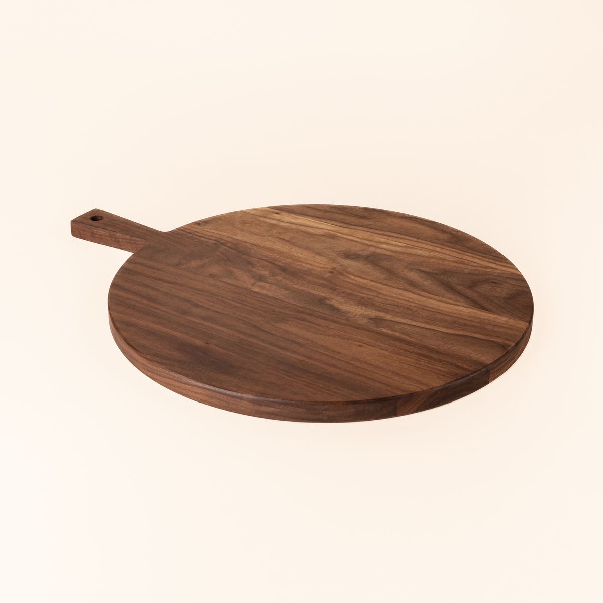 A round wooden serving board with a short rectangular handle with a hole for hanging