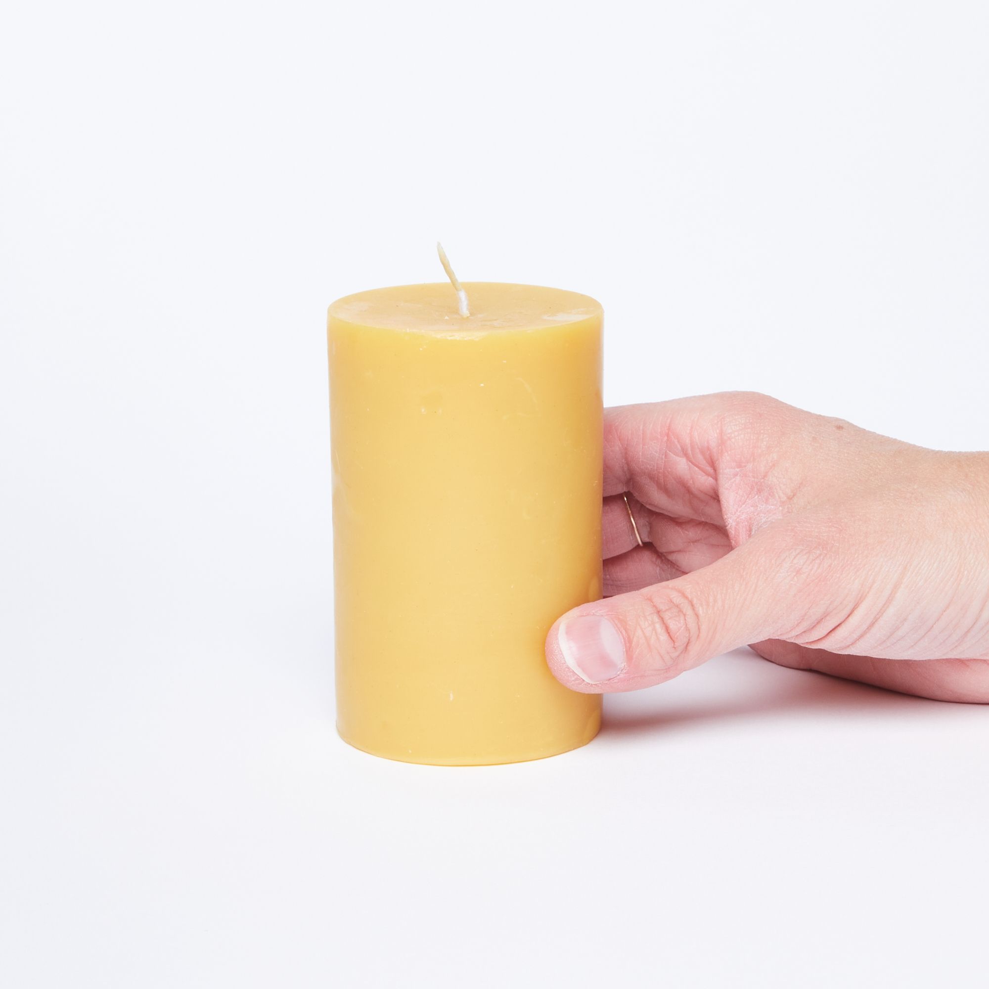 Hand holding a cylindrical yellow pillar candle