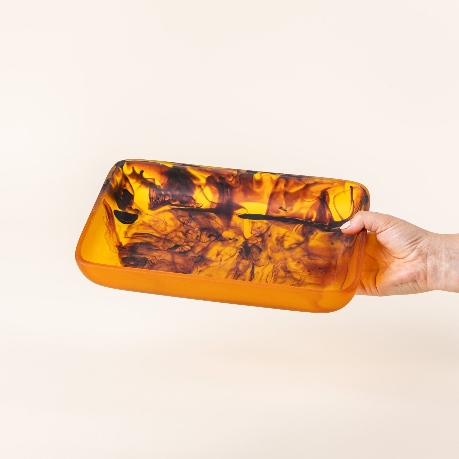 A hand holds a rectangular tortoiseshell tray with curved corners