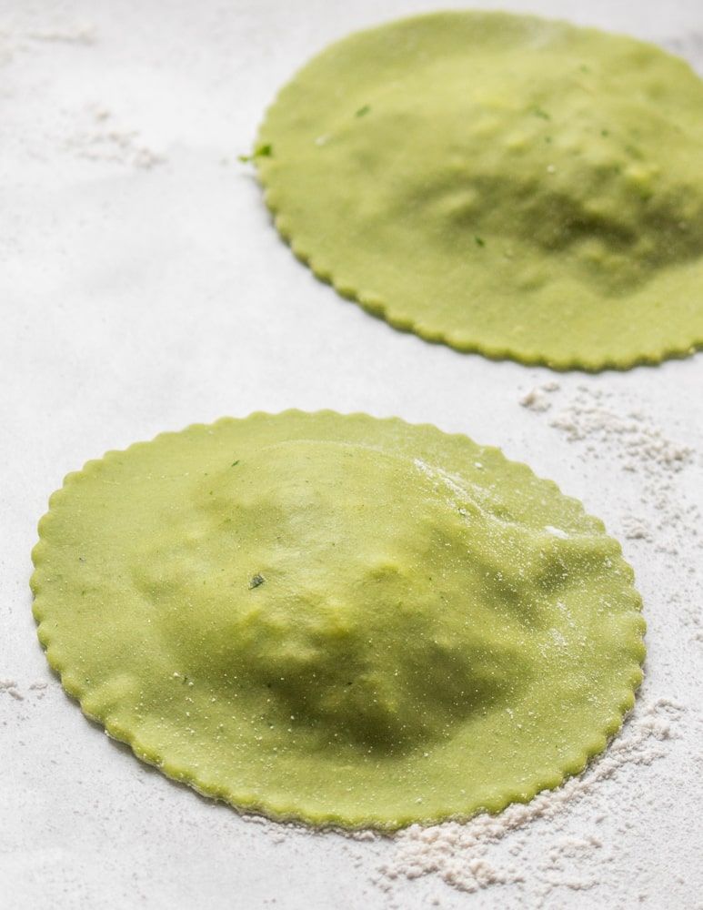 A closeup of round subtly scalloped green ravioli in the process of being made.